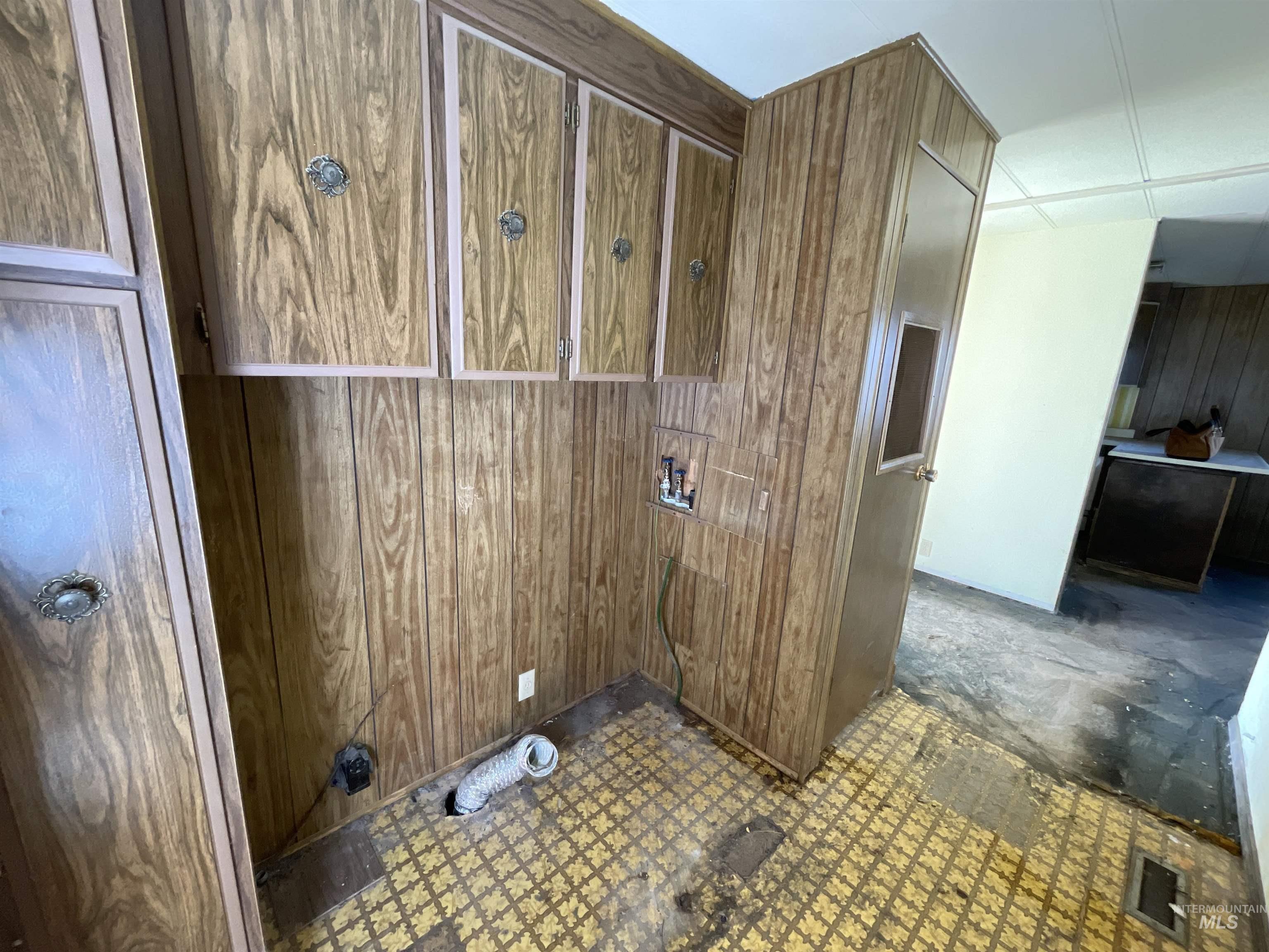 Laundry area featuring wooden walls and dark floors