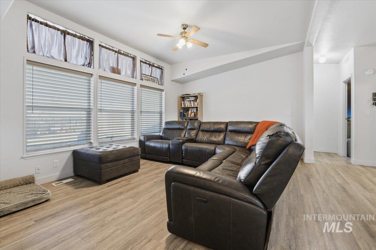Living area featuring ceiling fan, light wood-type flooring, and vaulted ceiling