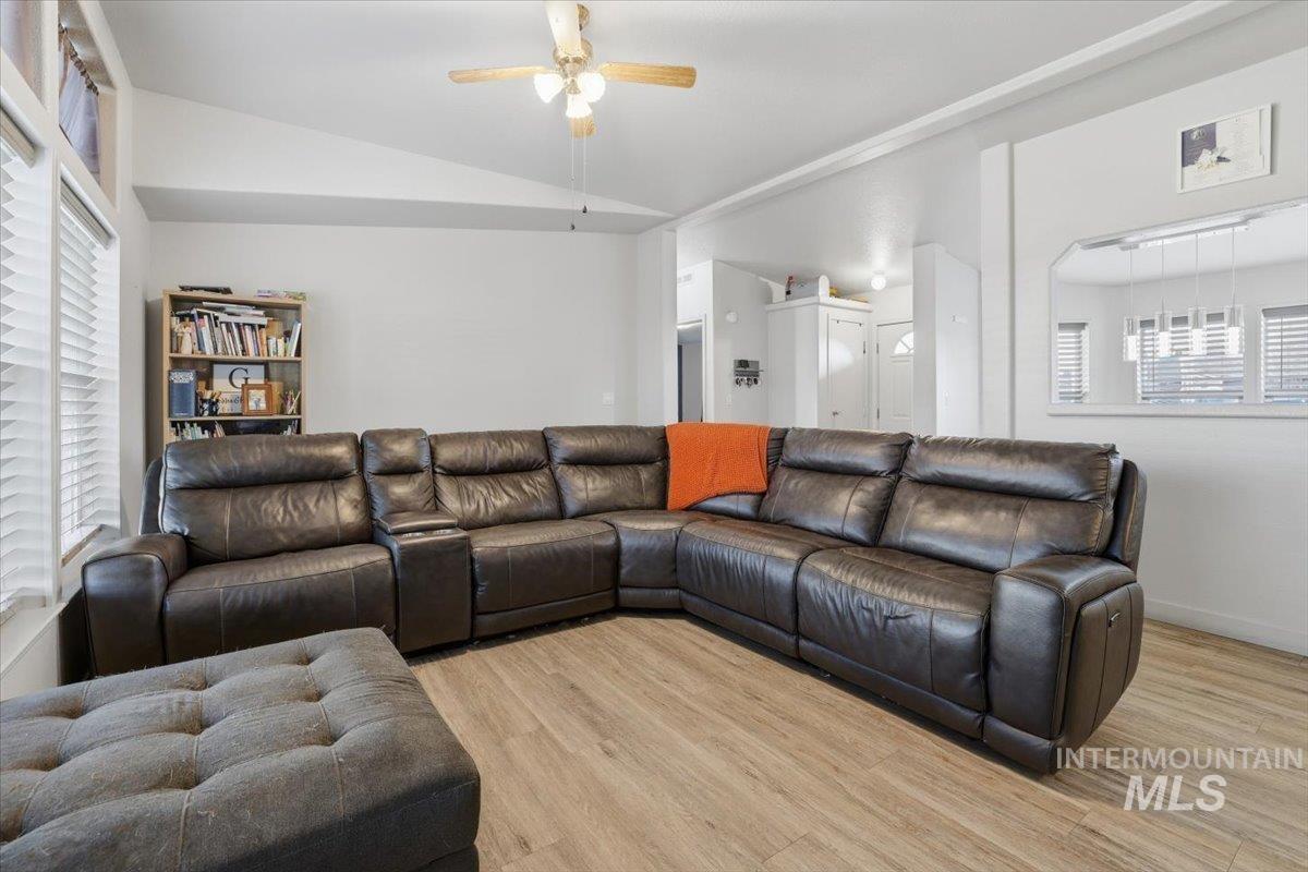 Living room with healthy amount of natural light, lofted ceiling, light wood-style flooring, and ceiling fan