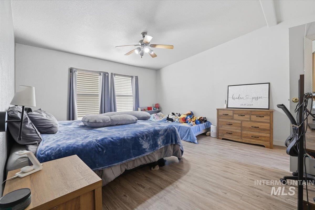 Bedroom featuring light wood-style floors, a ceiling fan, a textured ceiling, and lofted ceiling