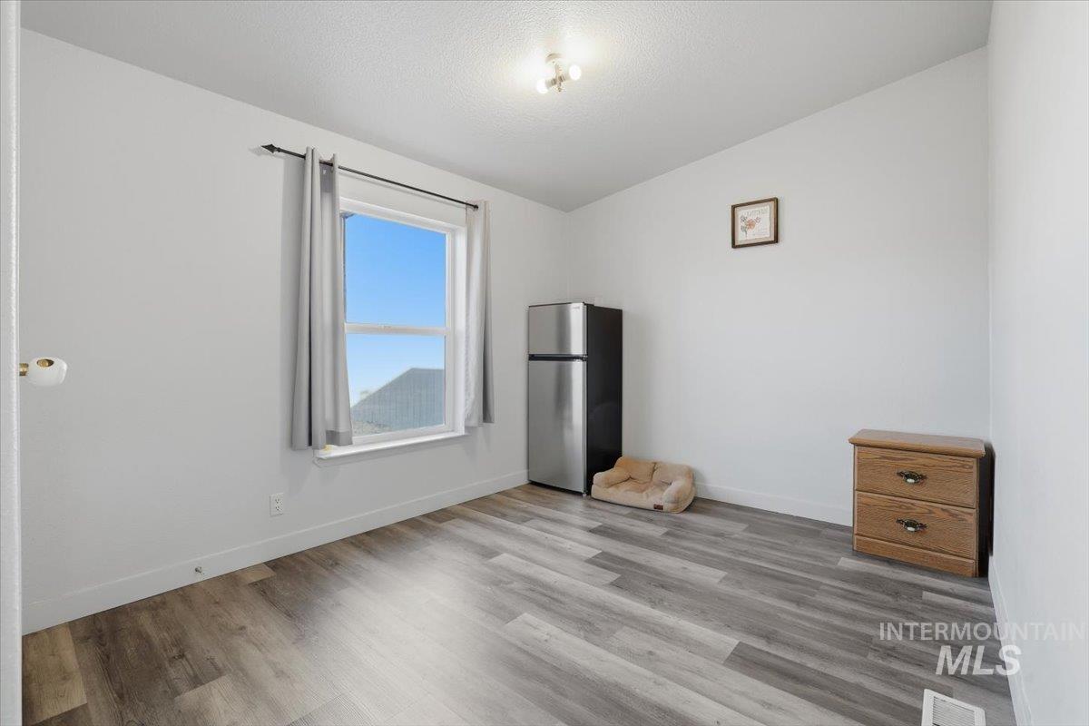 Unfurnished bedroom with freestanding refrigerator, lofted ceiling, wood finished floors, and a textured ceiling
