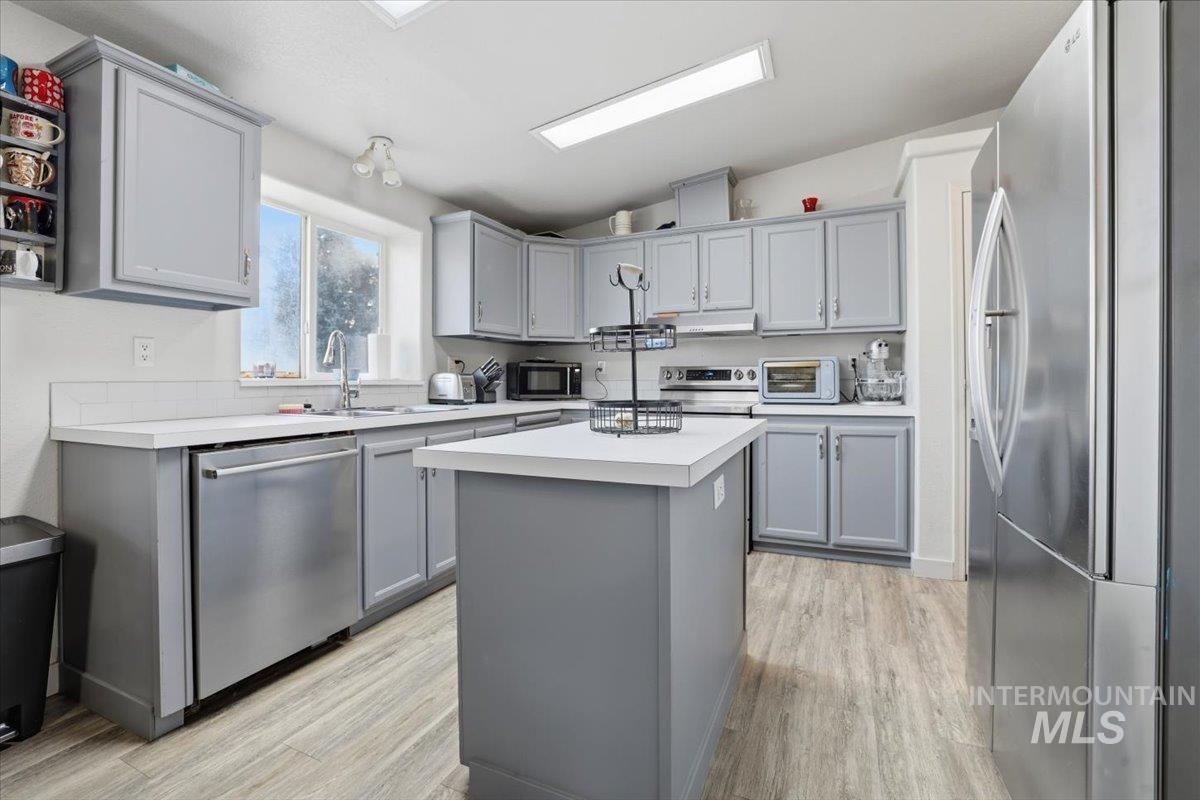 Kitchen with gray cabinetry, stainless steel appliances, light countertops, and lofted ceiling