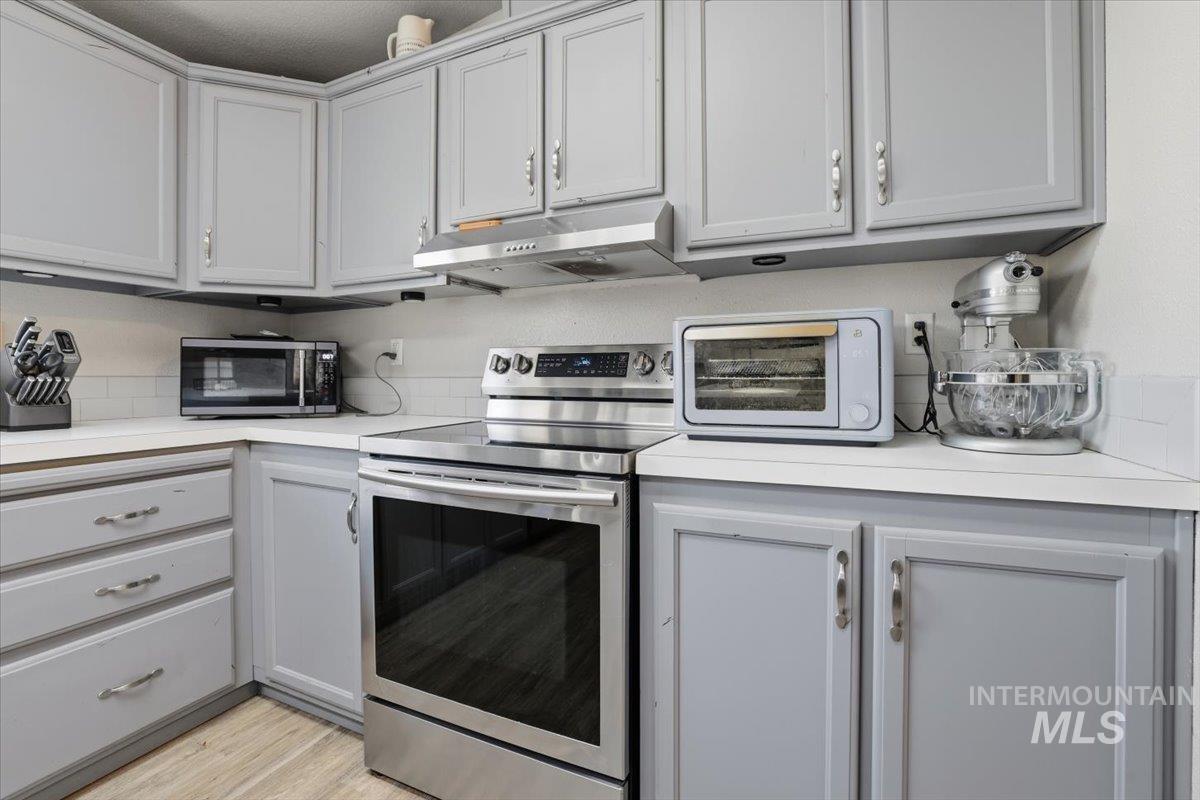 Kitchen featuring appliances with stainless steel finishes, light countertops, gray cabinetry, under cabinet range hood, and light wood finished floors