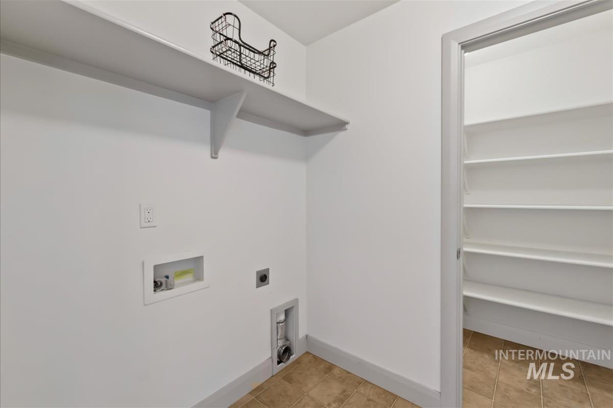 Laundry area with electric dryer hookup, hookup for a washing machine, and light tile patterned floors