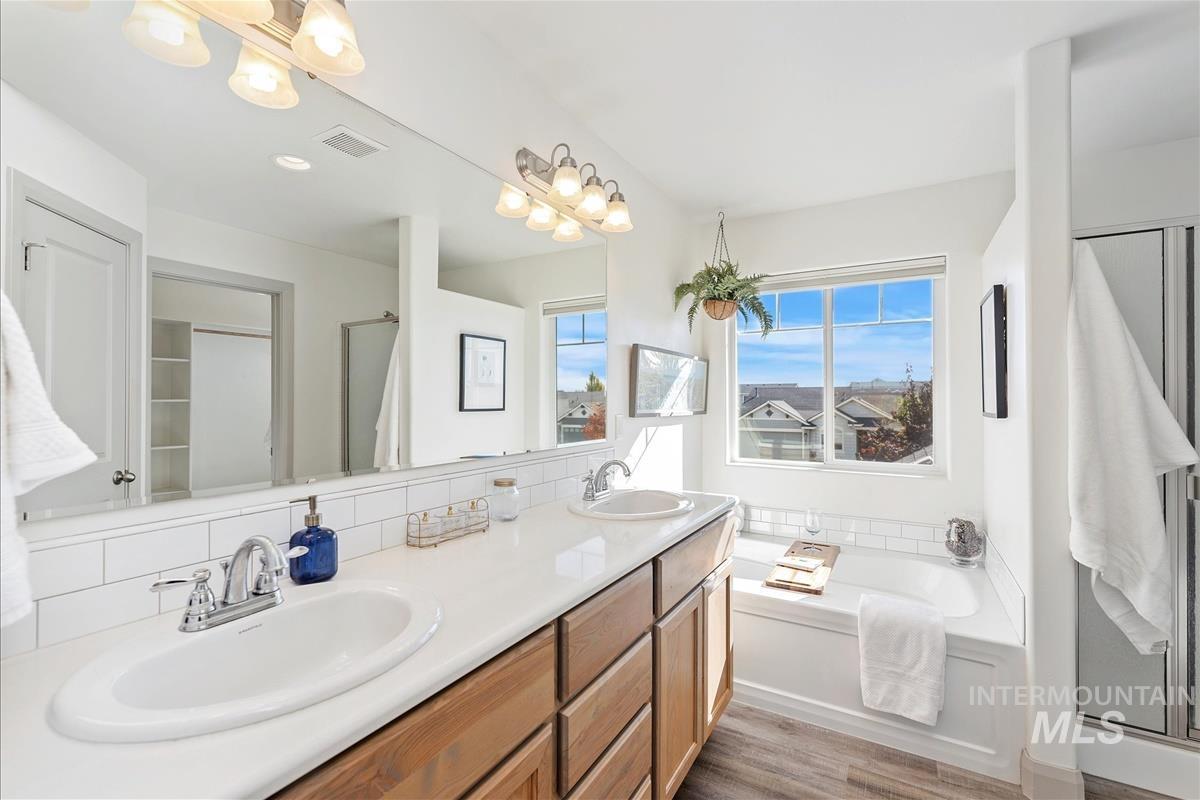 Full bath featuring double vanity, a shower stall, a bath, and light wood-style flooring