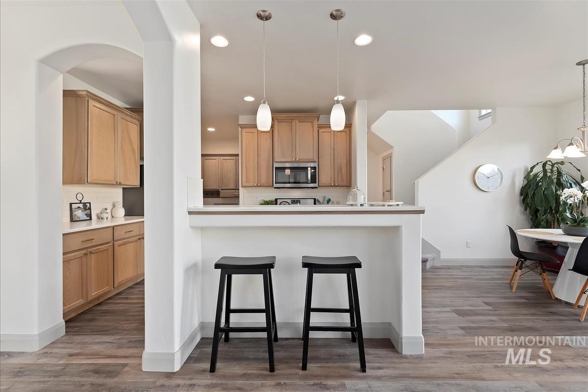 Kitchen with a breakfast bar, stainless steel microwave, light countertops, light wood-style floors, and recessed lighting
