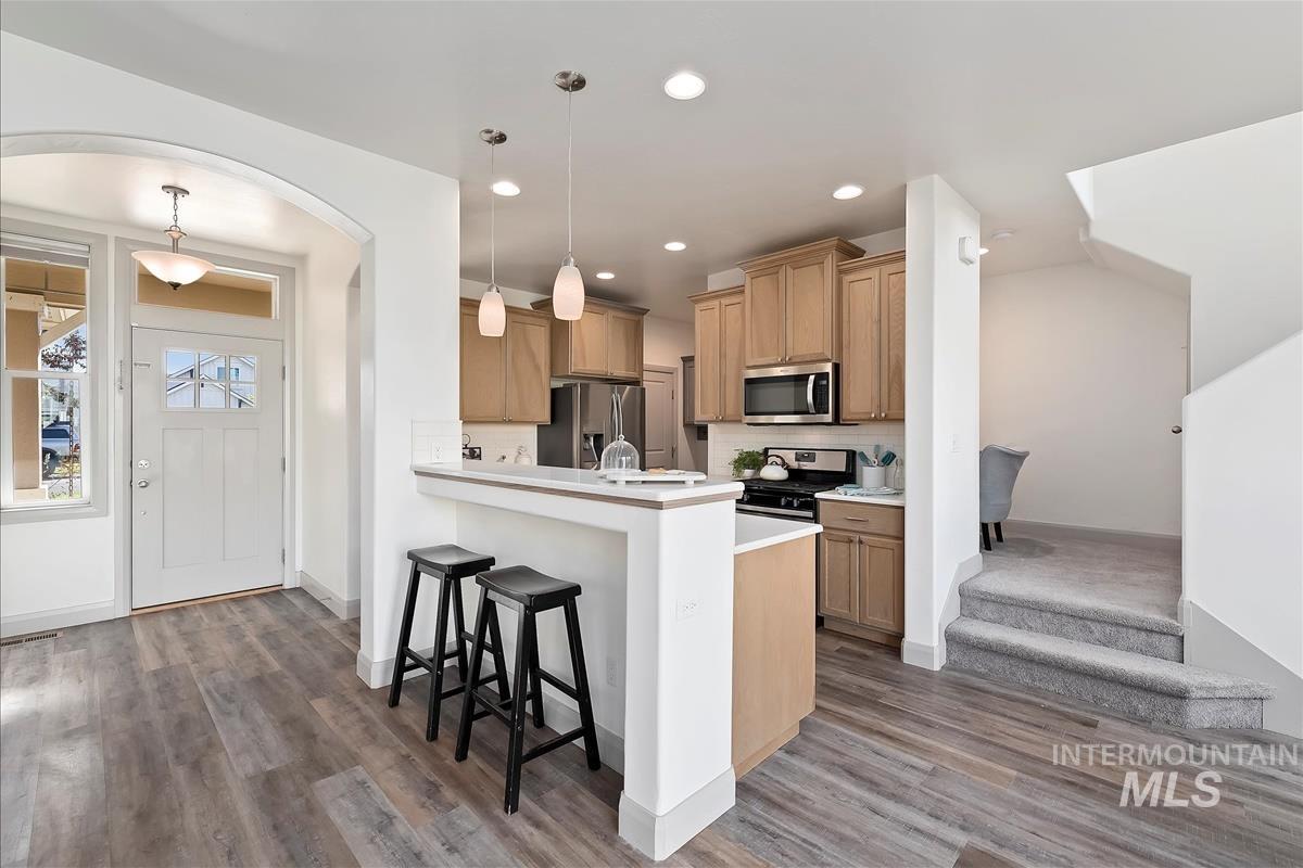 Kitchen with light countertops, a breakfast bar, hanging light fixtures, stainless steel appliances, and a peninsula