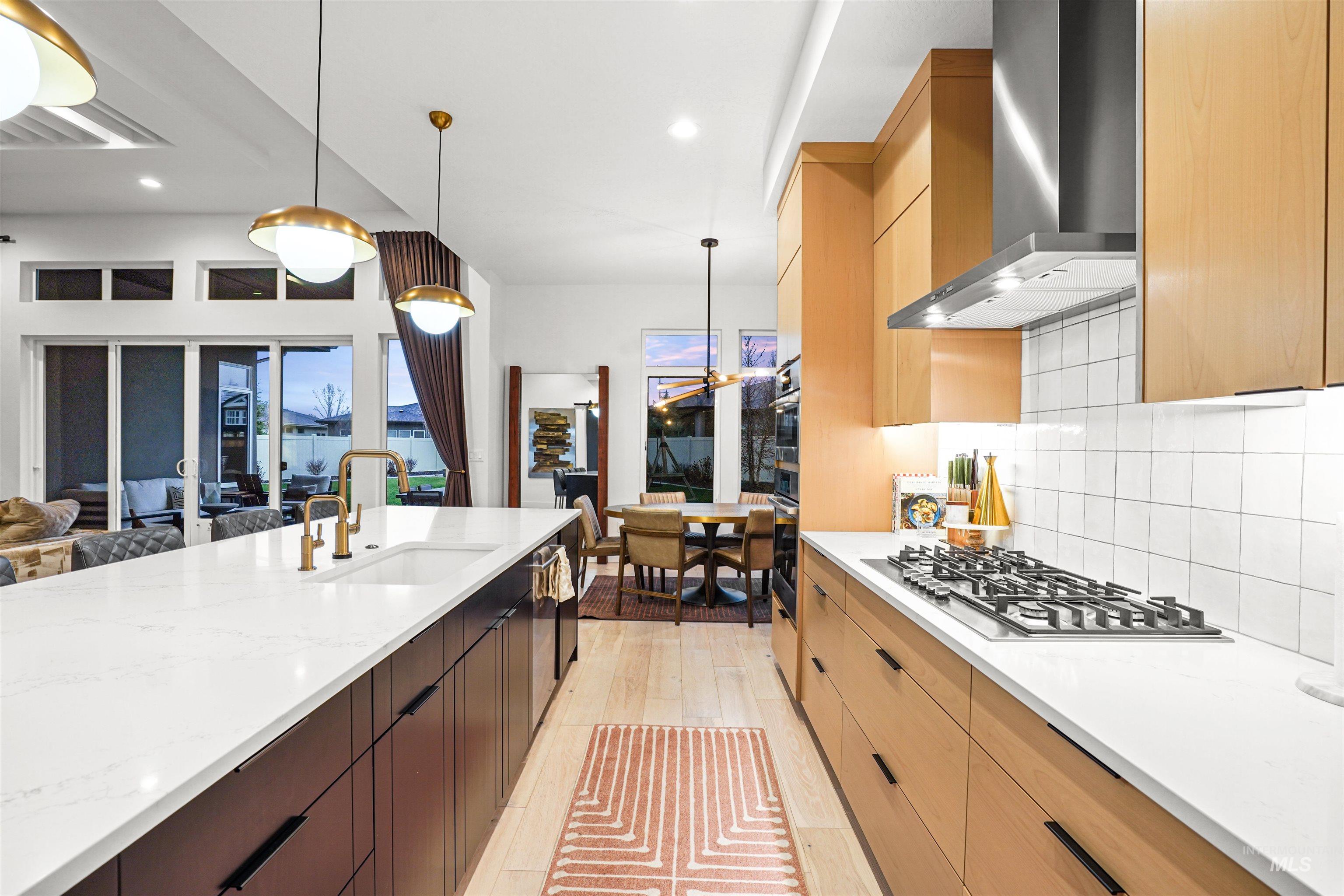 Kitchen featuring pendant lighting, light stone countertops, wall chimney range hood, tasteful backsplash, and modern cabinets