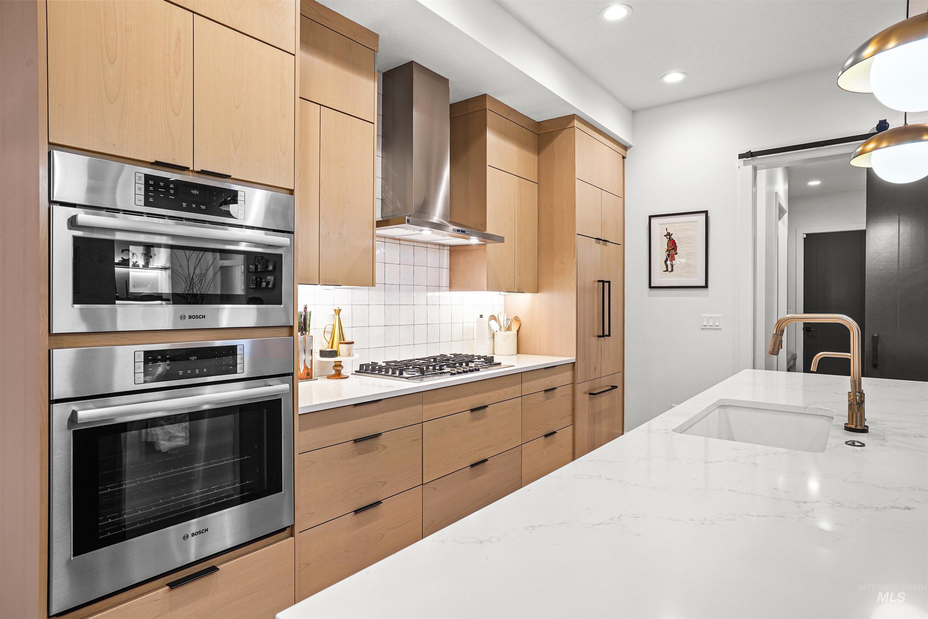 Kitchen with modern cabinets, decorative backsplash, appliances with stainless steel finishes, a barn door, and wall chimney exhaust hood