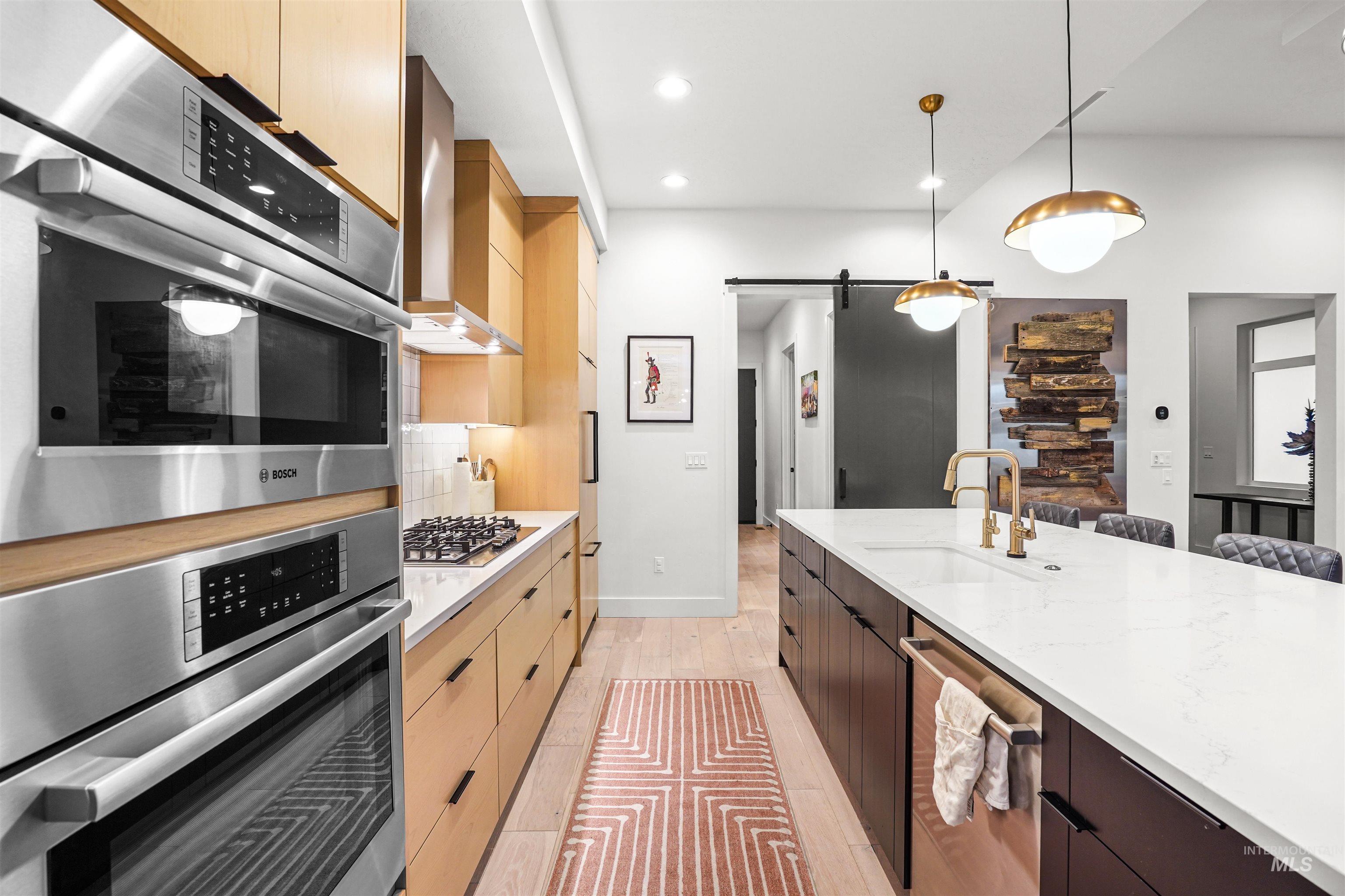 Kitchen featuring a barn door, modern cabinets, decorative light fixtures, light stone counters, and dark brown cabinets