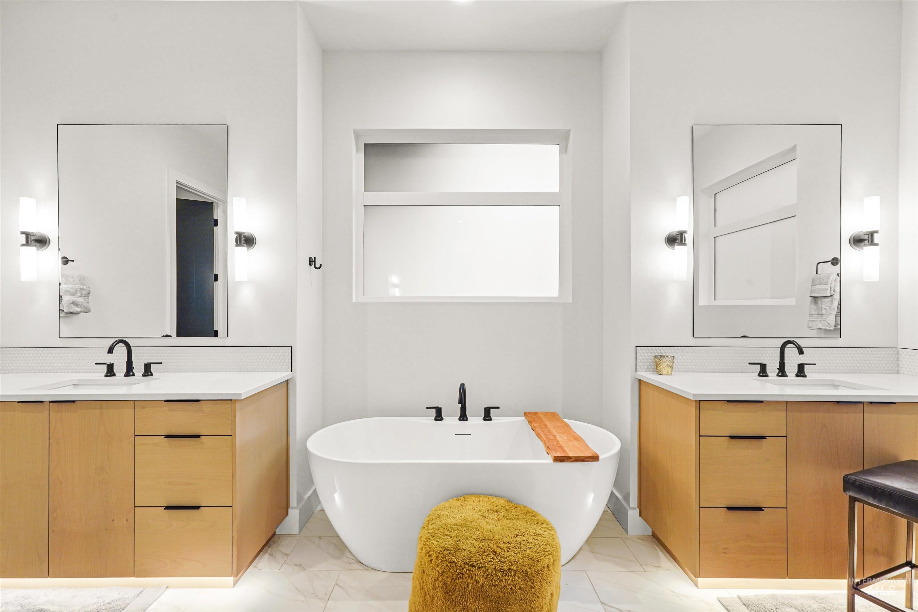 Full bathroom featuring light marble finish floors, a freestanding tub, two vanities, and backsplash