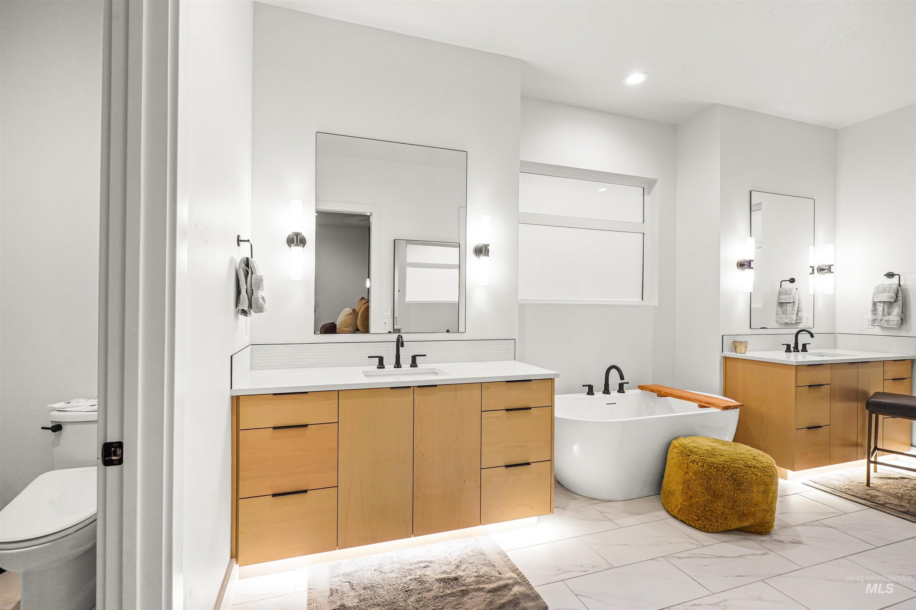 Bathroom featuring two vanities, a freestanding tub, light marble finish flooring, and recessed lighting