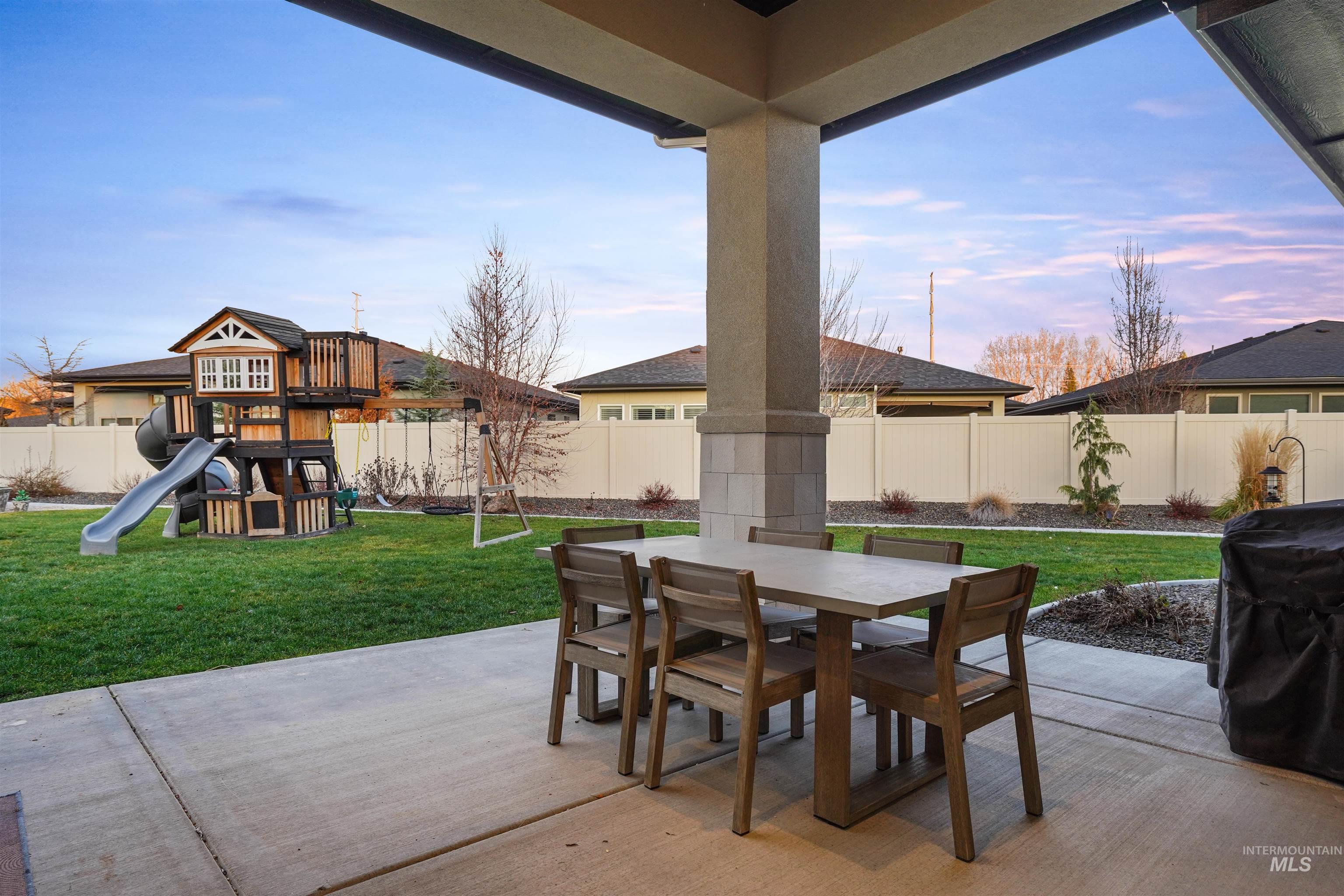 Patio terrace at dusk featuring outdoor dining space, a fenced backyard, a patio, and a playground