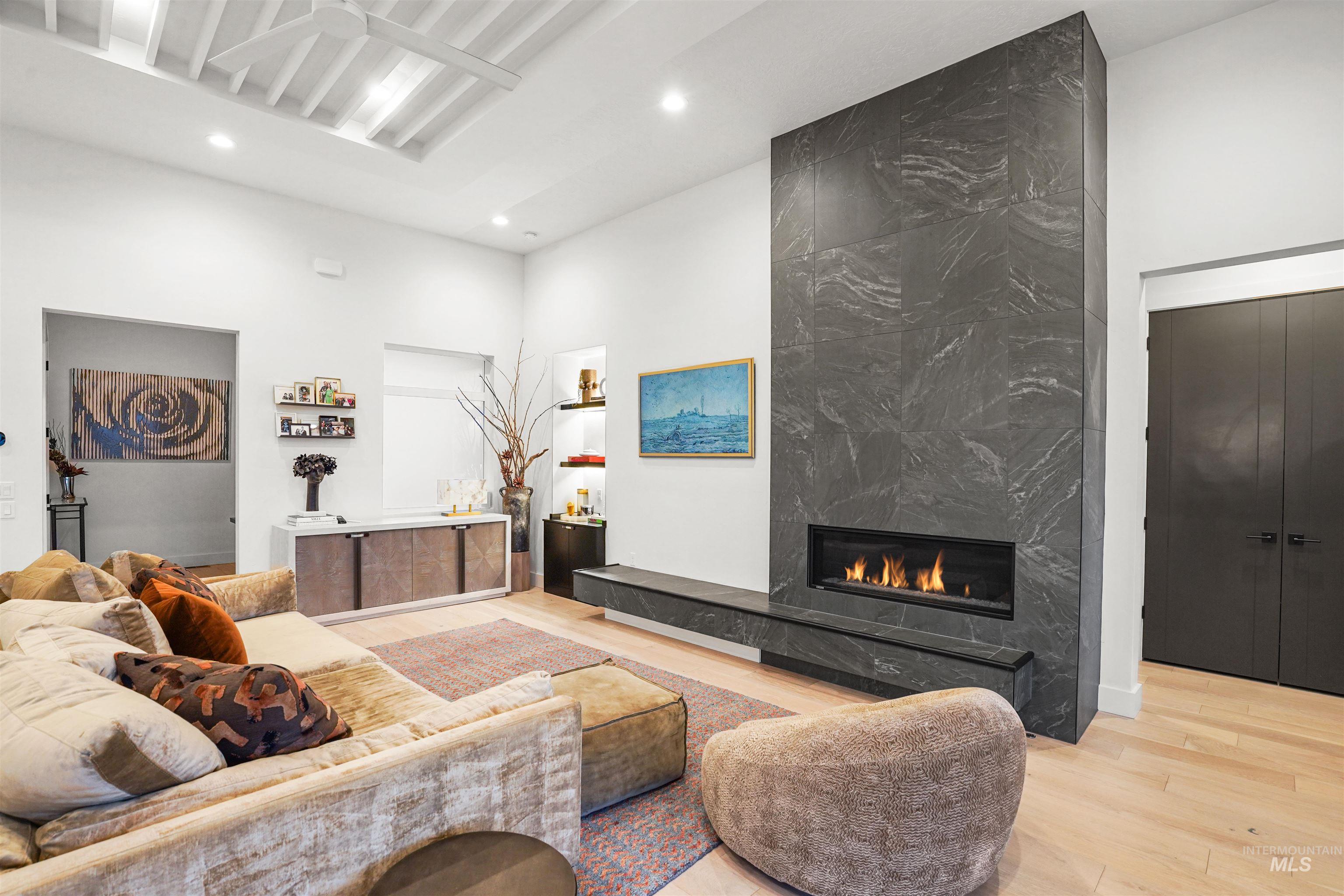 Living room with a fireplace, light wood finished floors, recessed lighting, and a high ceiling