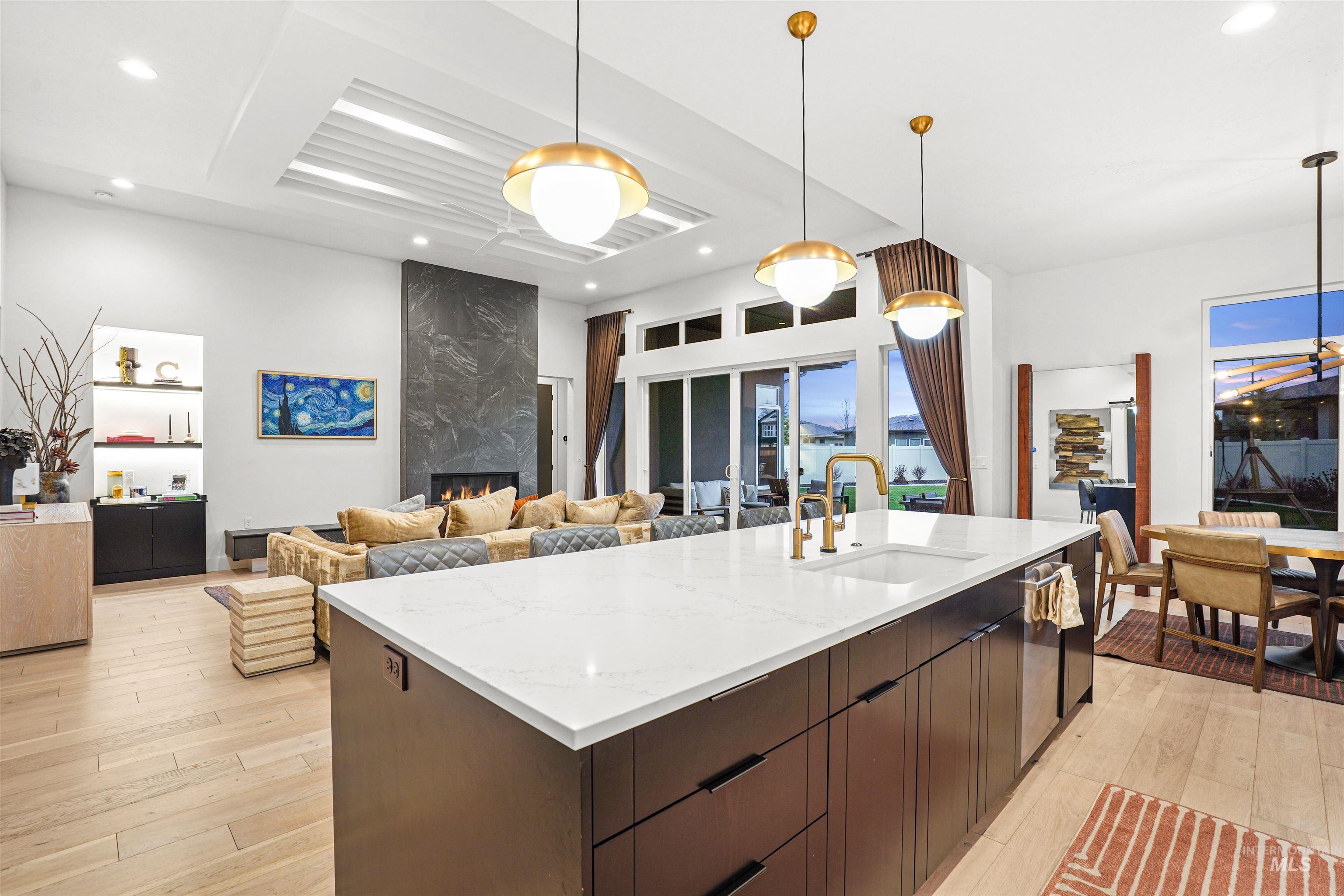 Kitchen featuring decorative light fixtures, dark brown cabinetry, light stone counters, open floor plan, and a high end fireplace