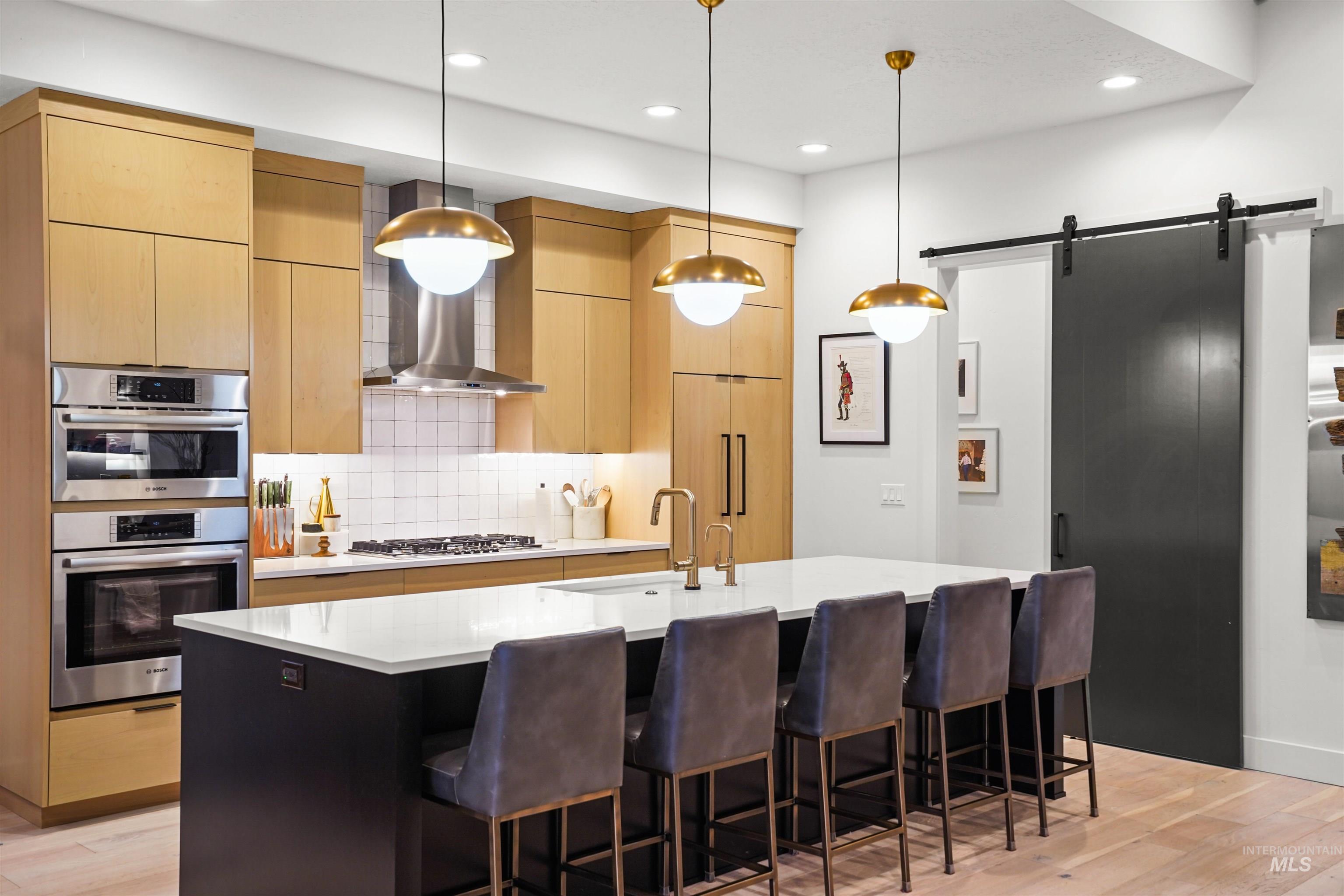 Kitchen featuring modern cabinets, a barn door, tasteful backsplash, decorative light fixtures, and a kitchen island with sink