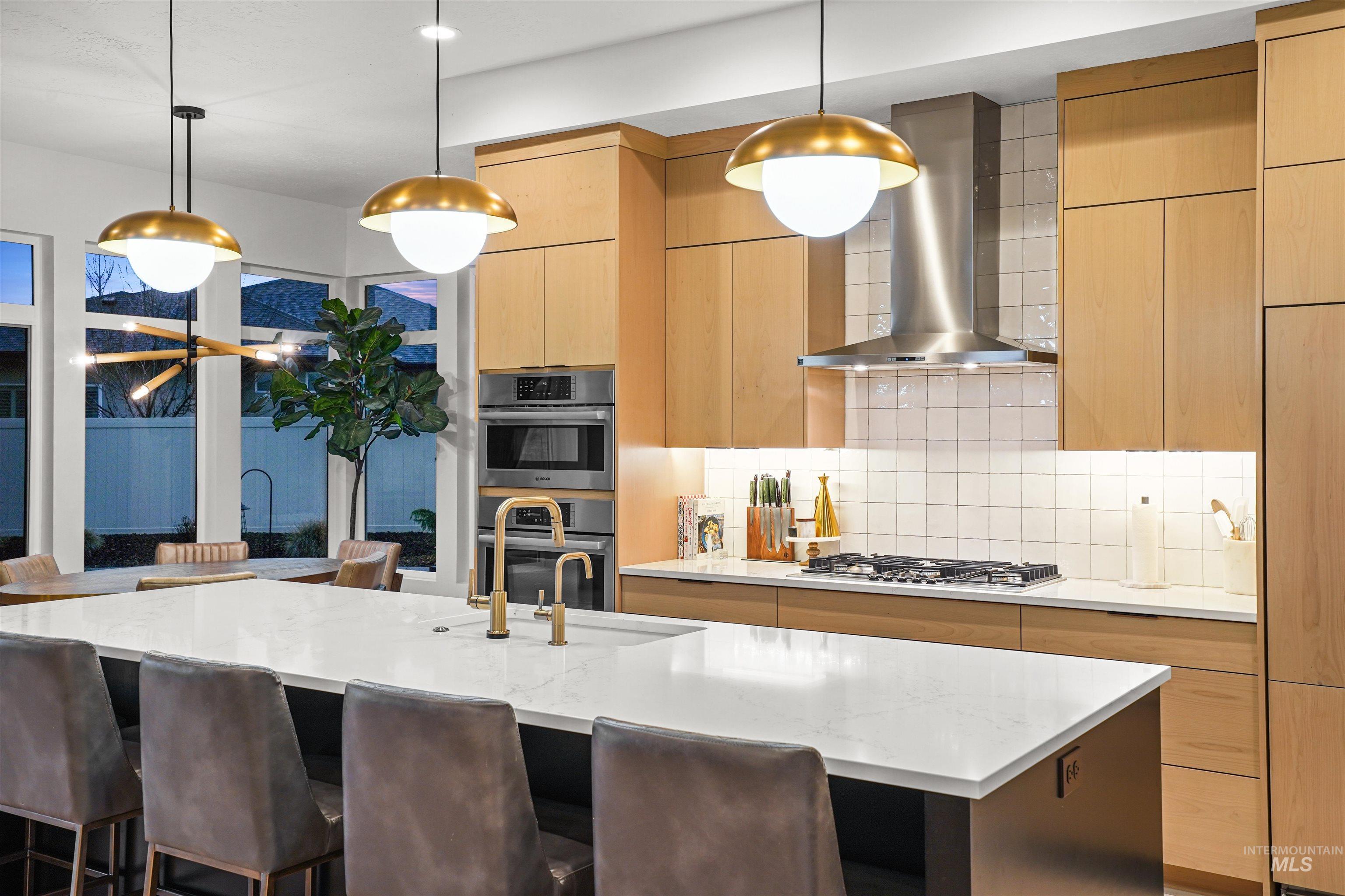 Kitchen featuring decorative backsplash, modern cabinets, wall chimney range hood, light brown cabinetry, and light stone counters