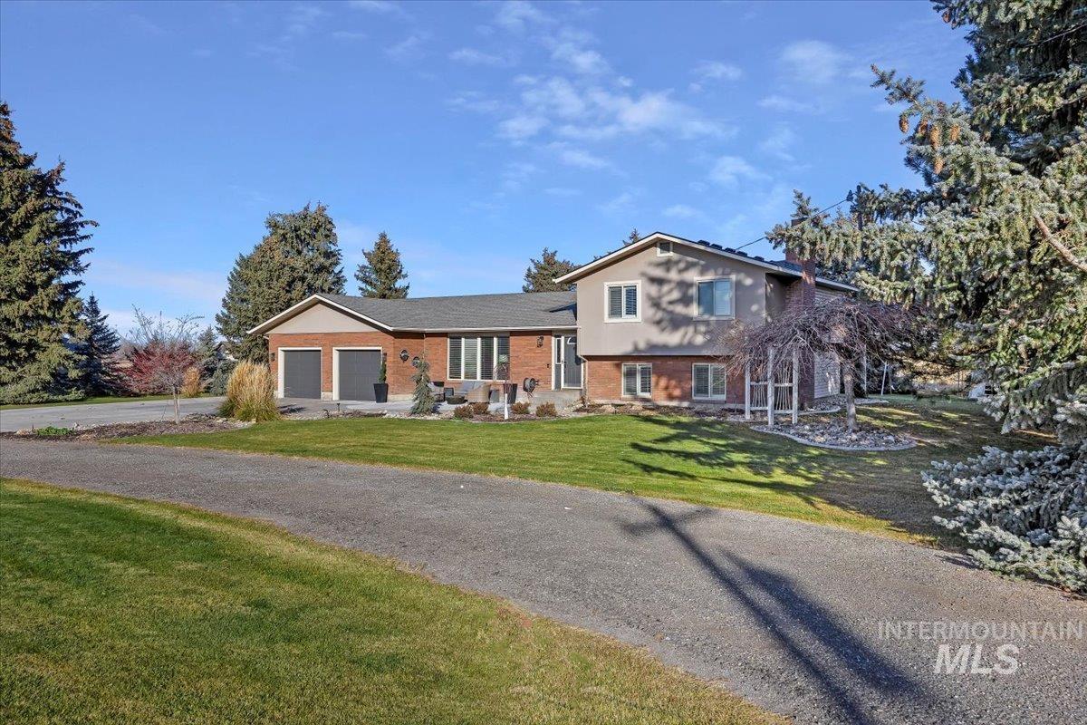 Split level home with a front yard, brick siding, an attached garage, and driveway