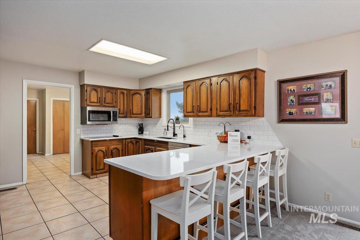 Kitchen with a breakfast bar area, a peninsula, brown cabinetry, backsplash, and stainless steel microwave
