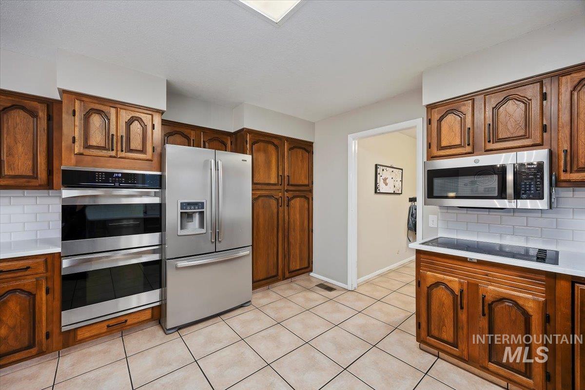 Kitchen featuring backsplash, appliances with stainless steel finishes, and brown cabinets