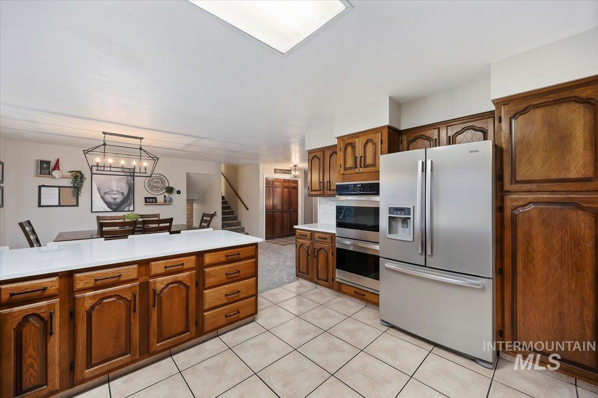 Kitchen featuring appliances with stainless steel finishes, pendant lighting, brown cabinets, and light stone counters