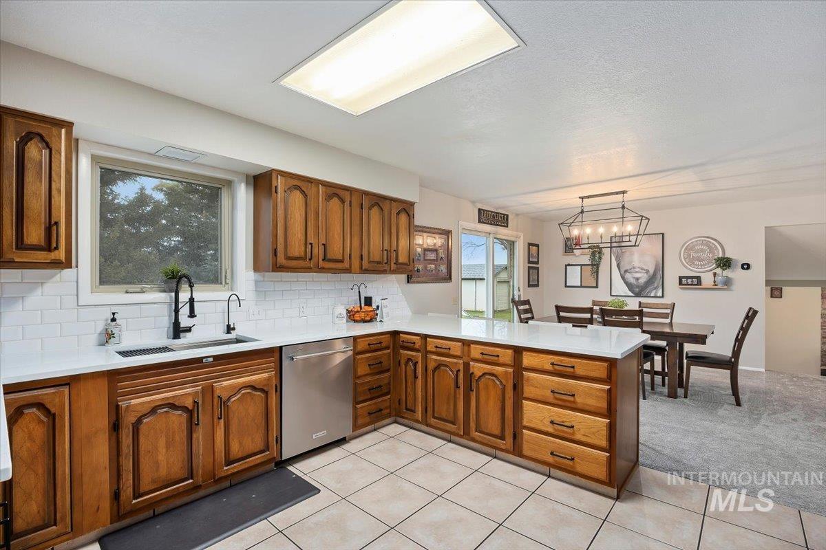 Kitchen with backsplash, a peninsula, brown cabinets, dishwasher, and light stone counters