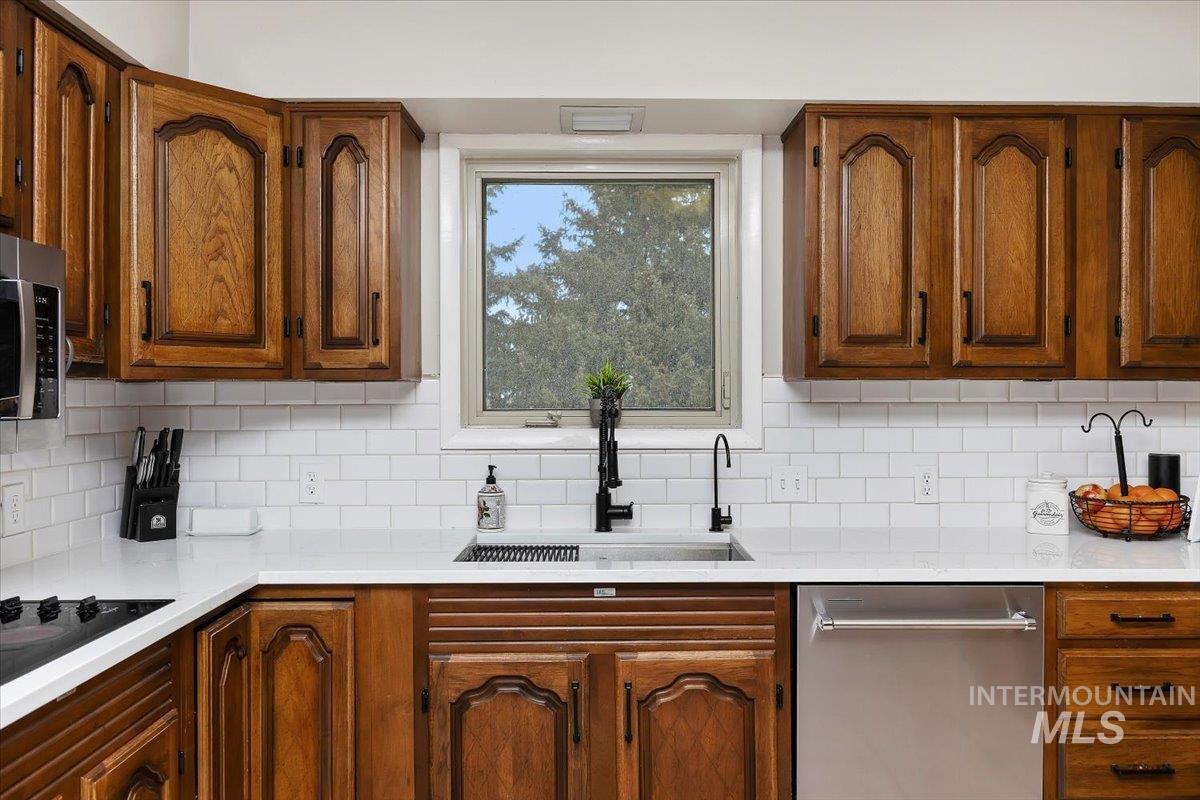 Kitchen with stainless steel appliances, brown cabinets, light stone countertops, and backsplash