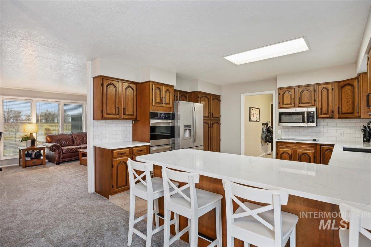 Kitchen featuring light stone counters, brown cabinetry, a peninsula, and a kitchen breakfast bar