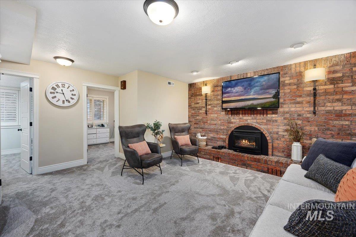 Living area featuring carpet, a textured ceiling, a fireplace, and brick wall