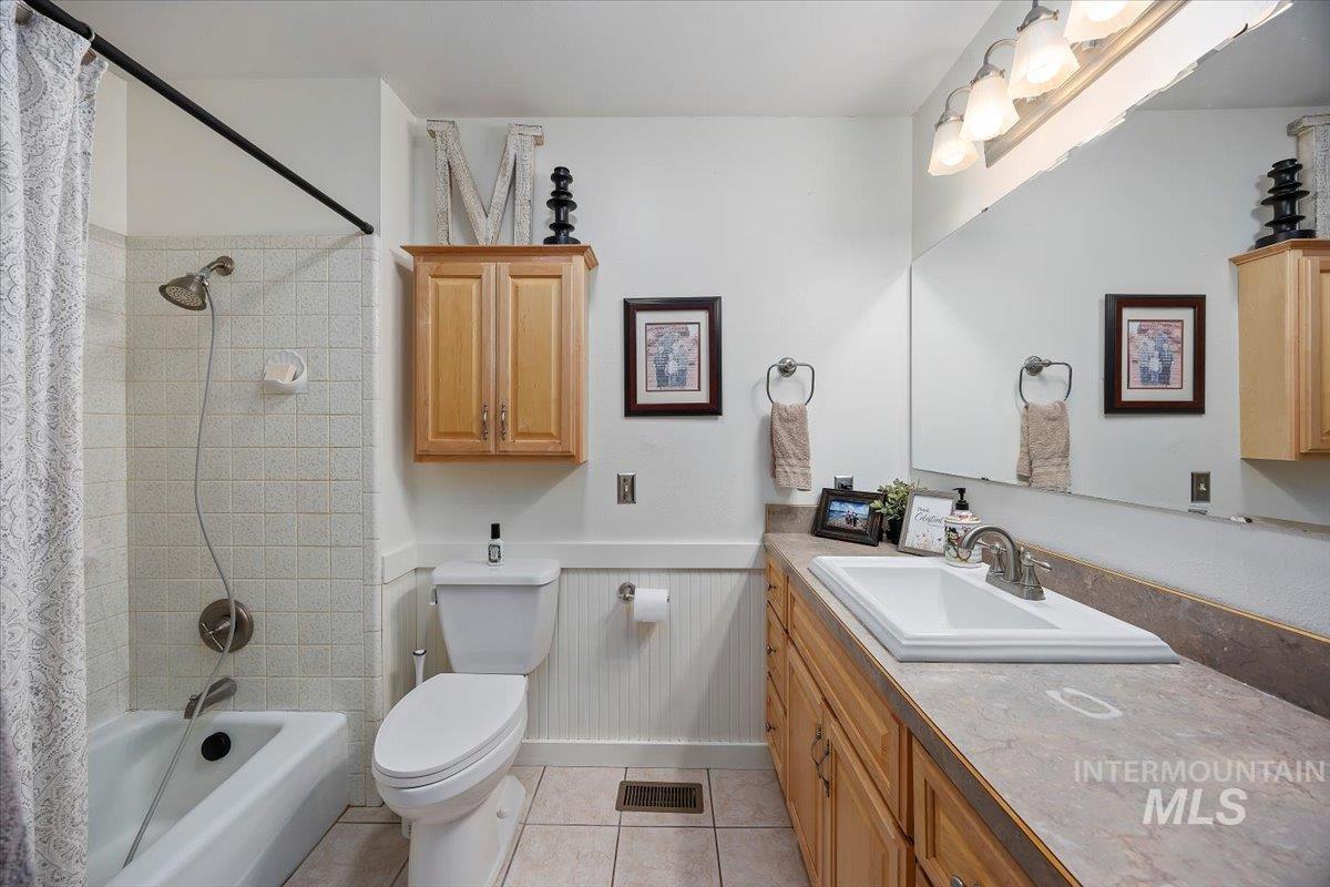Bathroom with wainscoting, shower / bath combo with shower curtain, vanity, and light tile patterned flooring