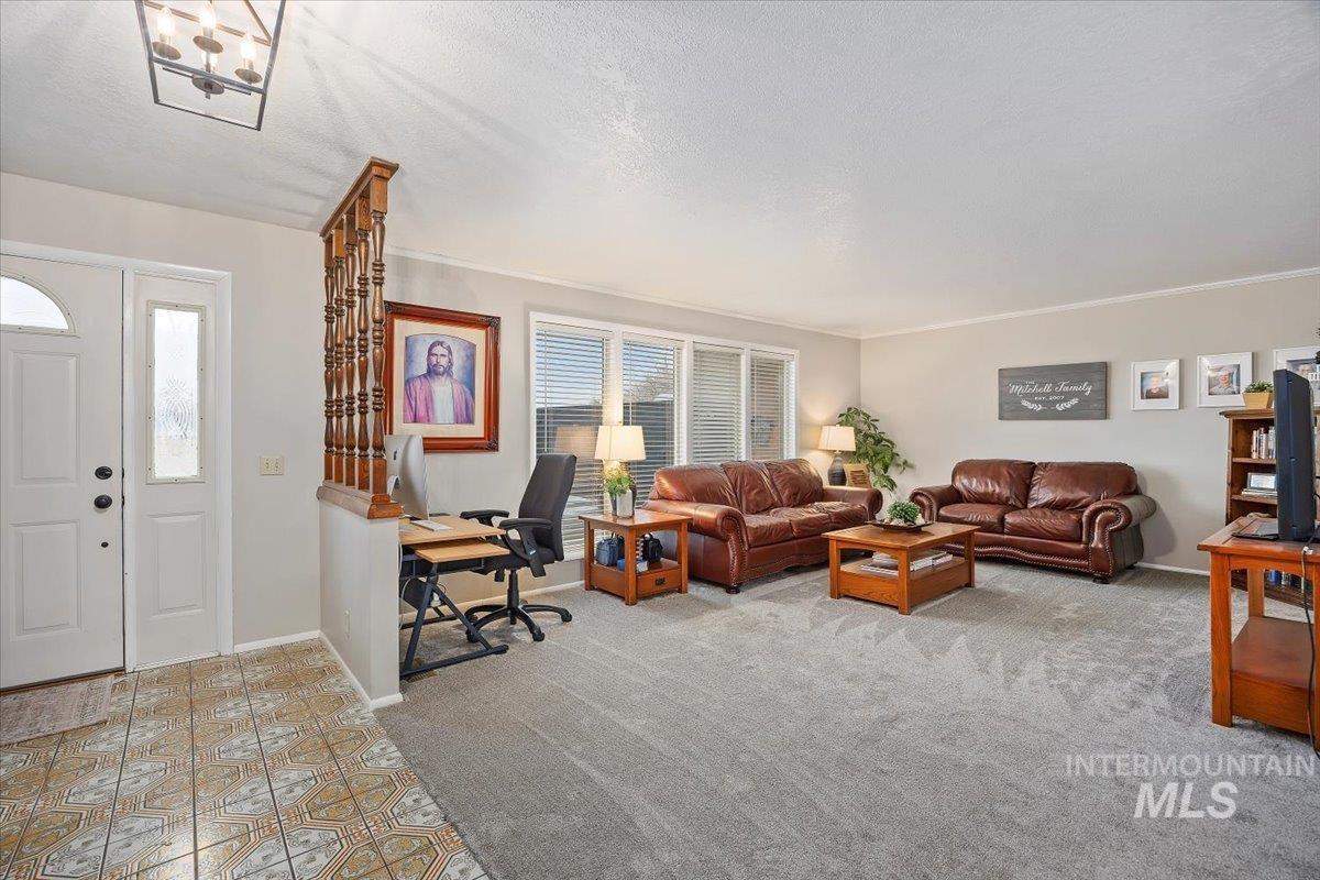 Living room with an office area, a textured ceiling, a chandelier, light carpet, and crown molding