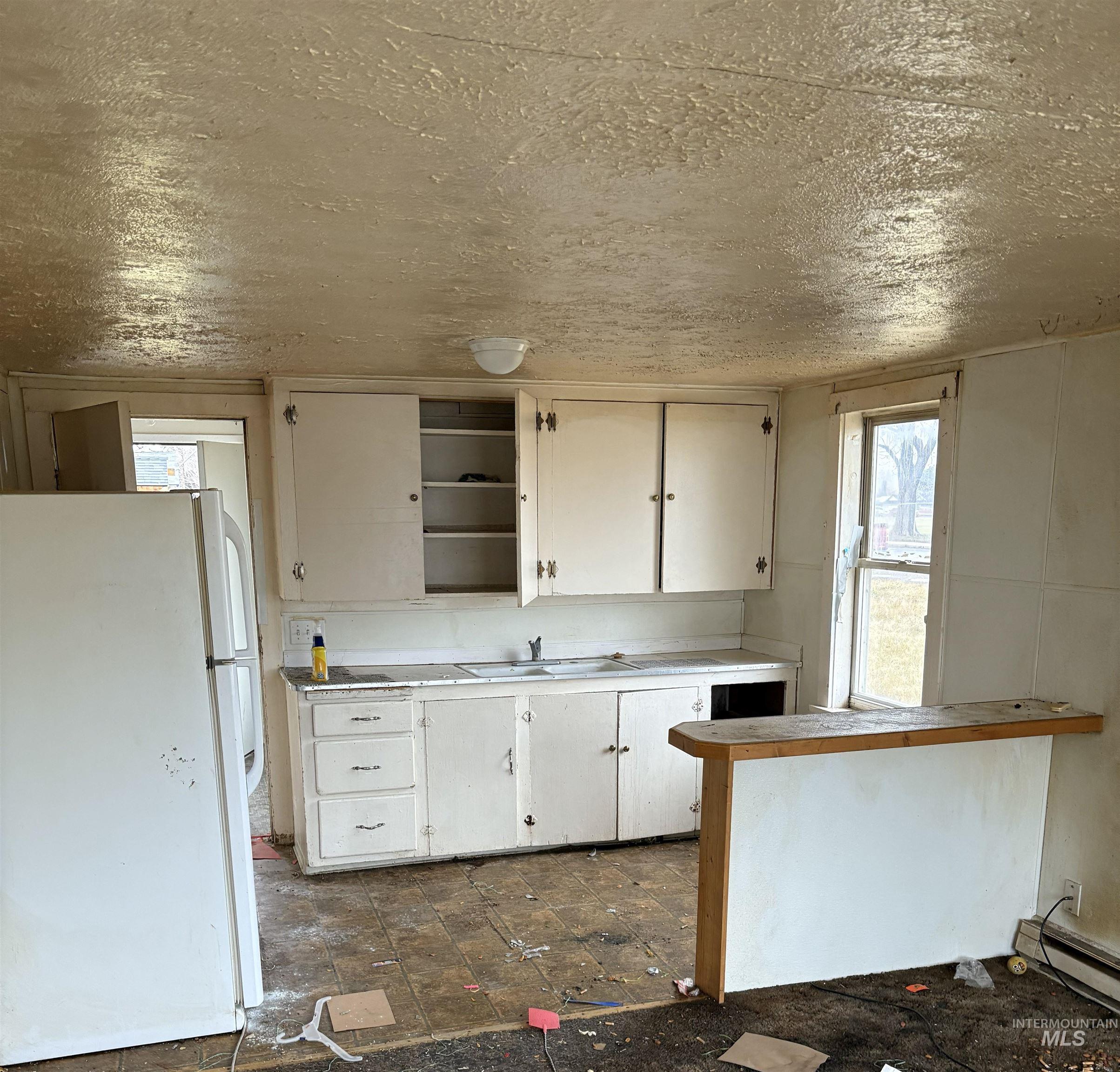 Kitchen featuring freestanding refrigerator, white cabinetry, light countertops, open shelves, and a textured ceiling