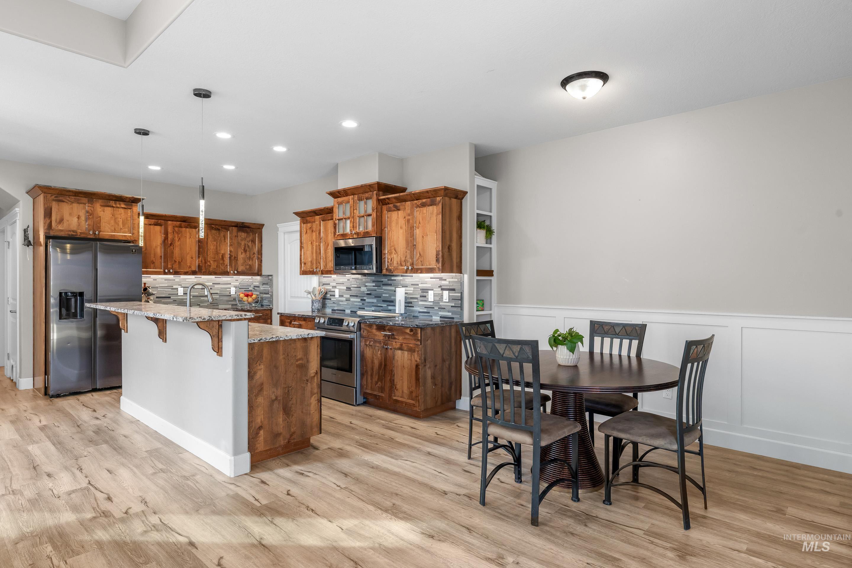 Kitchen with a kitchen breakfast bar, brown cabinetry, dark stone counters, decorative light fixtures, and stainless steel appliances