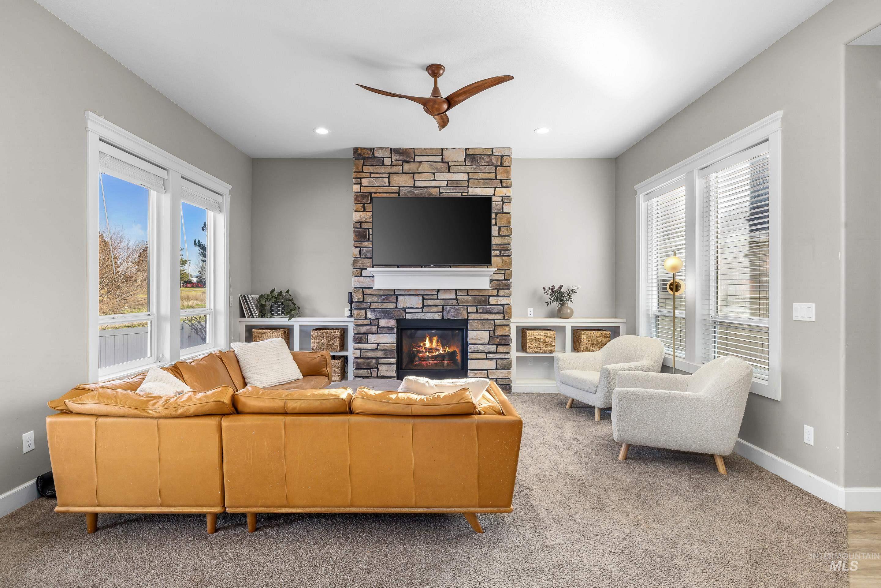 Living area featuring a stone fireplace, a ceiling fan, and carpet floors