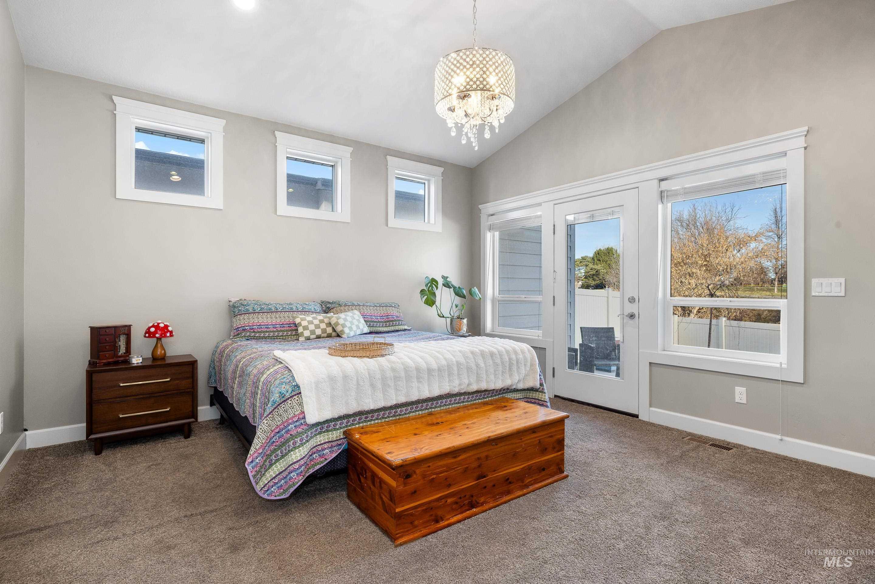 Carpeted bedroom with multiple windows, vaulted ceiling, access to exterior, and a chandelier