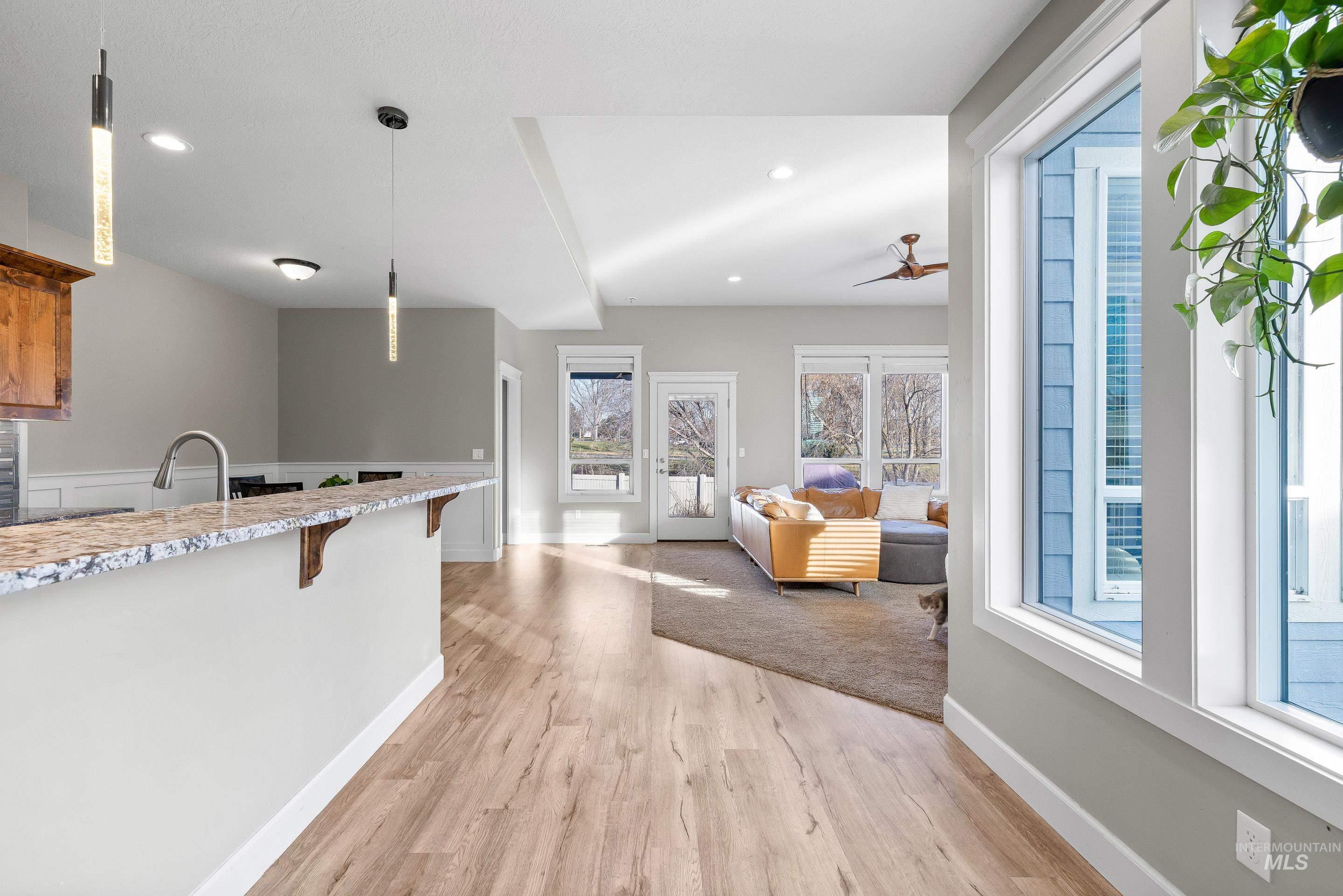 Kitchen featuring a kitchen bar, pendant lighting, light stone countertops, light wood-style floors, and a ceiling fan