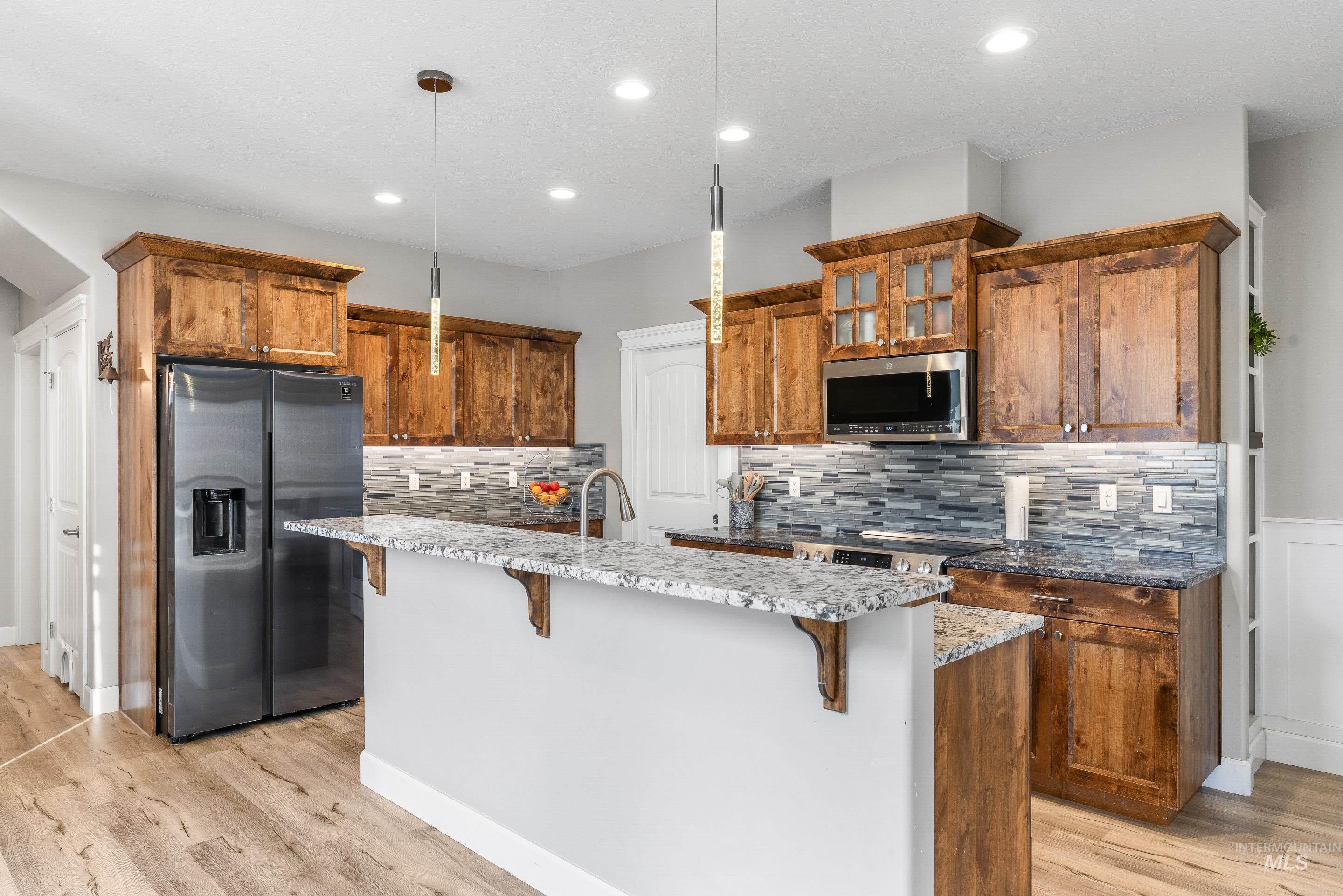 Kitchen featuring brown cabinetry, appliances with stainless steel finishes, backsplash, decorative light fixtures, and recessed lighting