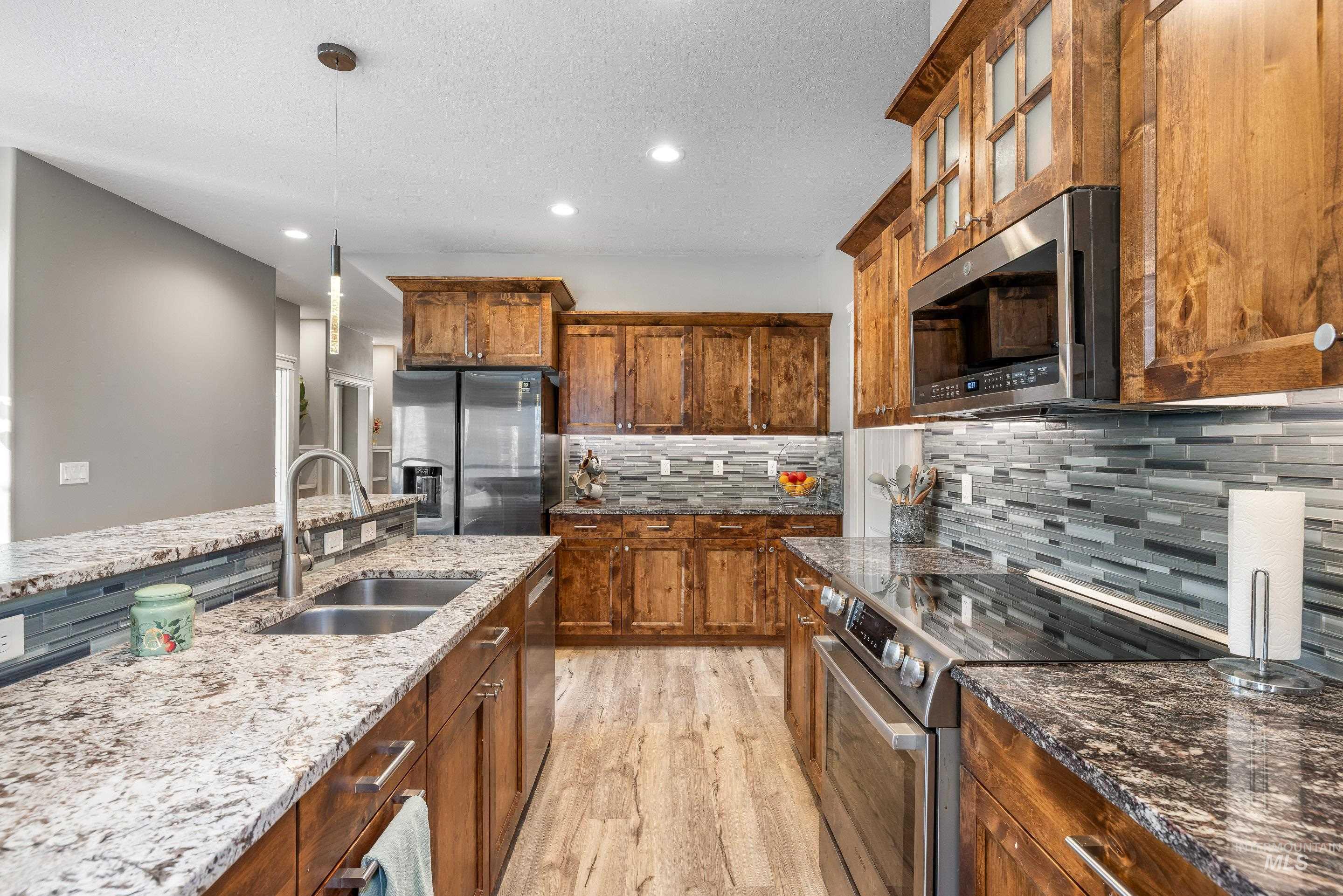 Kitchen with brown cabinets, stainless steel appliances, hanging light fixtures, dark stone counters, and light wood finished floors