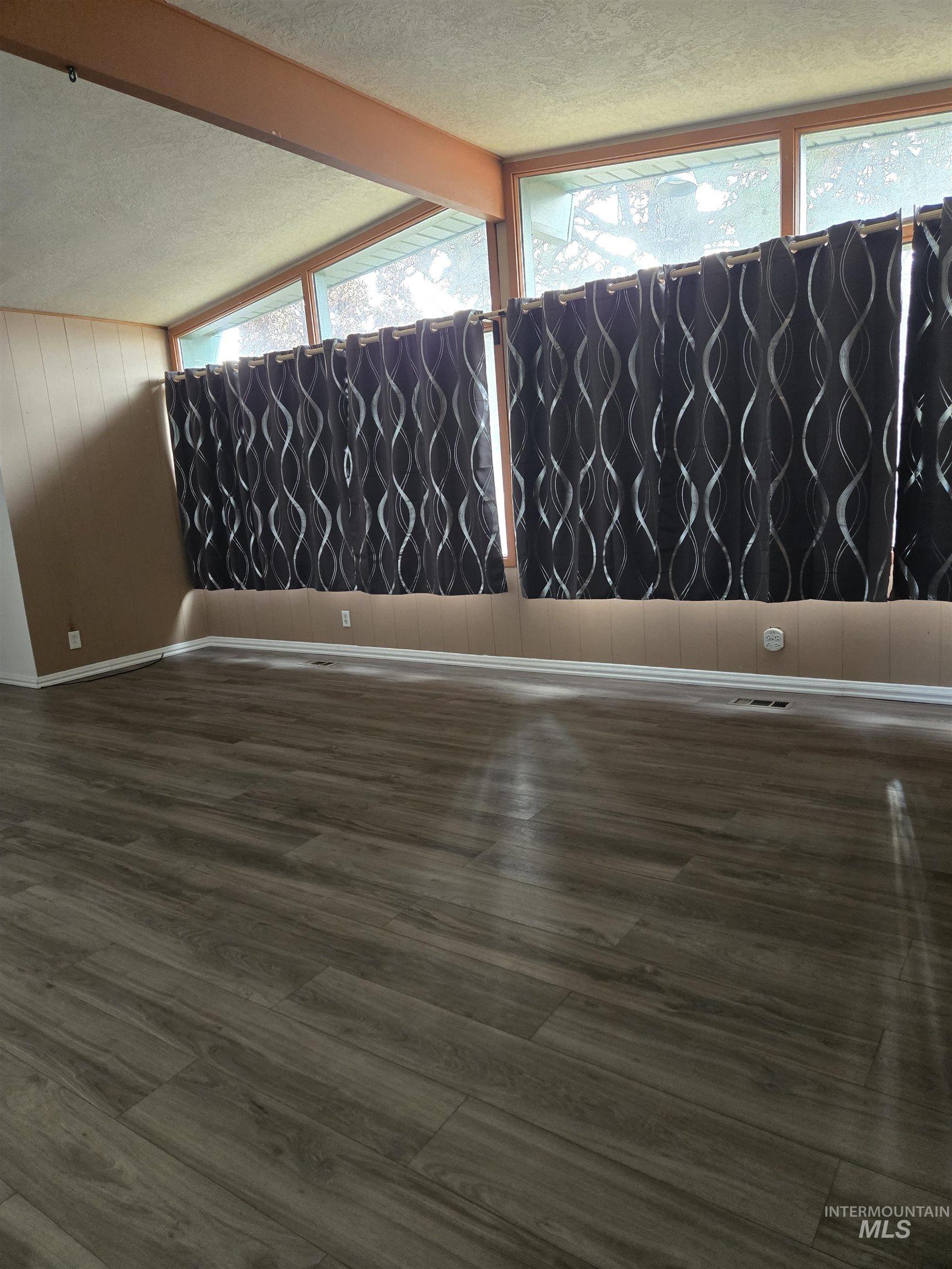 Spare room with a textured ceiling, wooden walls, and wood finished floors