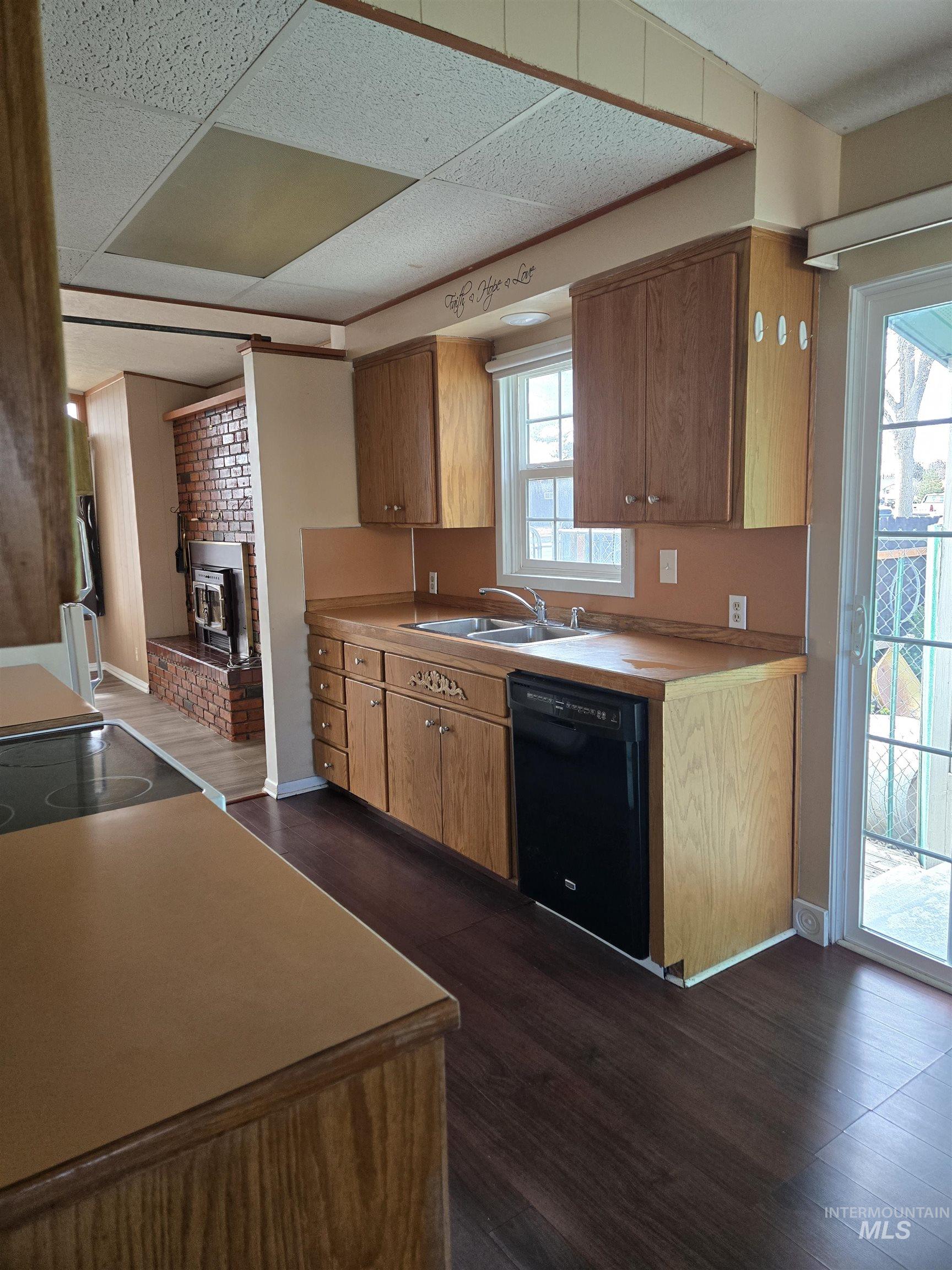 Kitchen featuring black dishwasher, brown cabinets, light countertops, electric range oven, and dark wood-type flooring