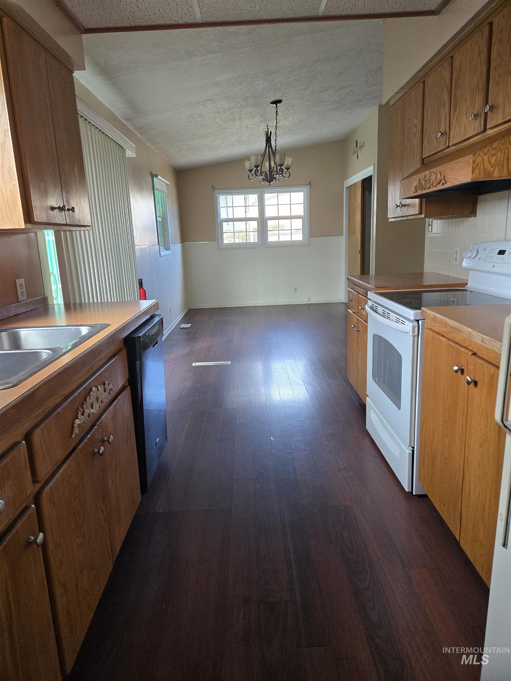Kitchen featuring white electric stove, wainscoting, under cabinet range hood, hanging light fixtures, and dishwashing machine