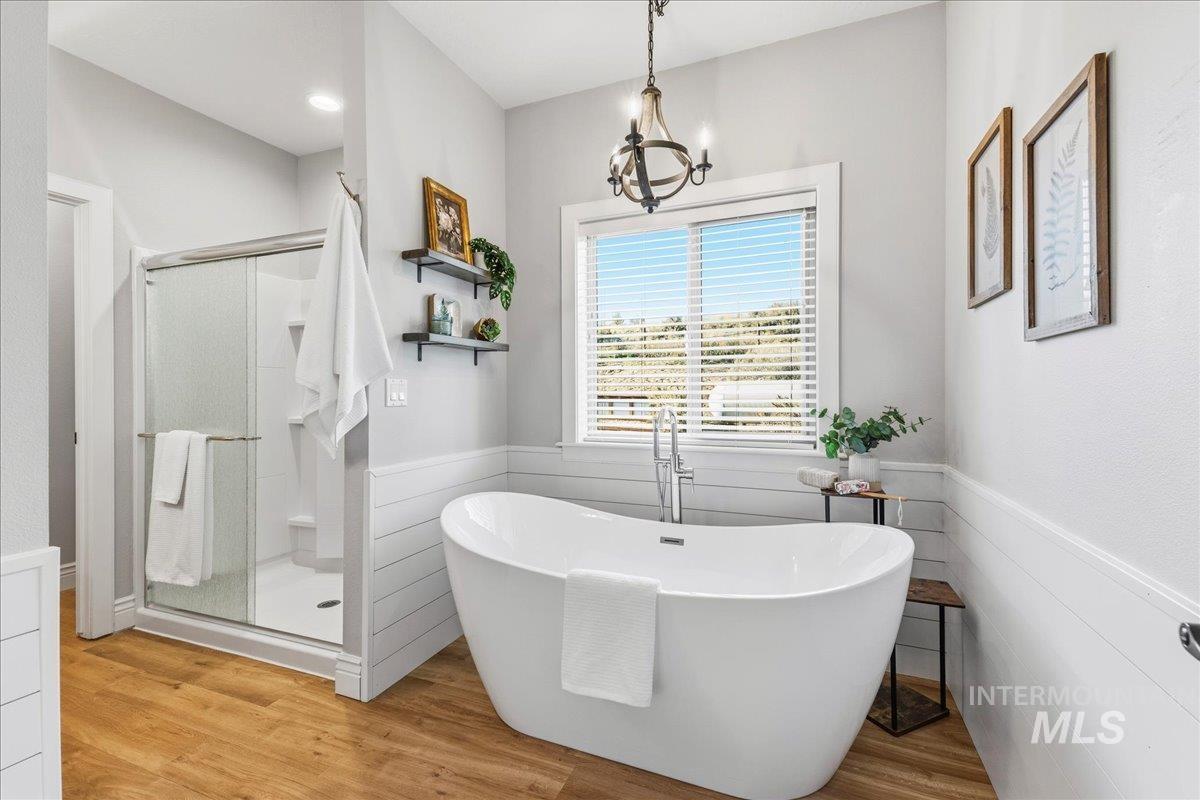 Bathroom with wainscoting, a shower stall, a freestanding tub, light wood-type flooring, and a chandelier