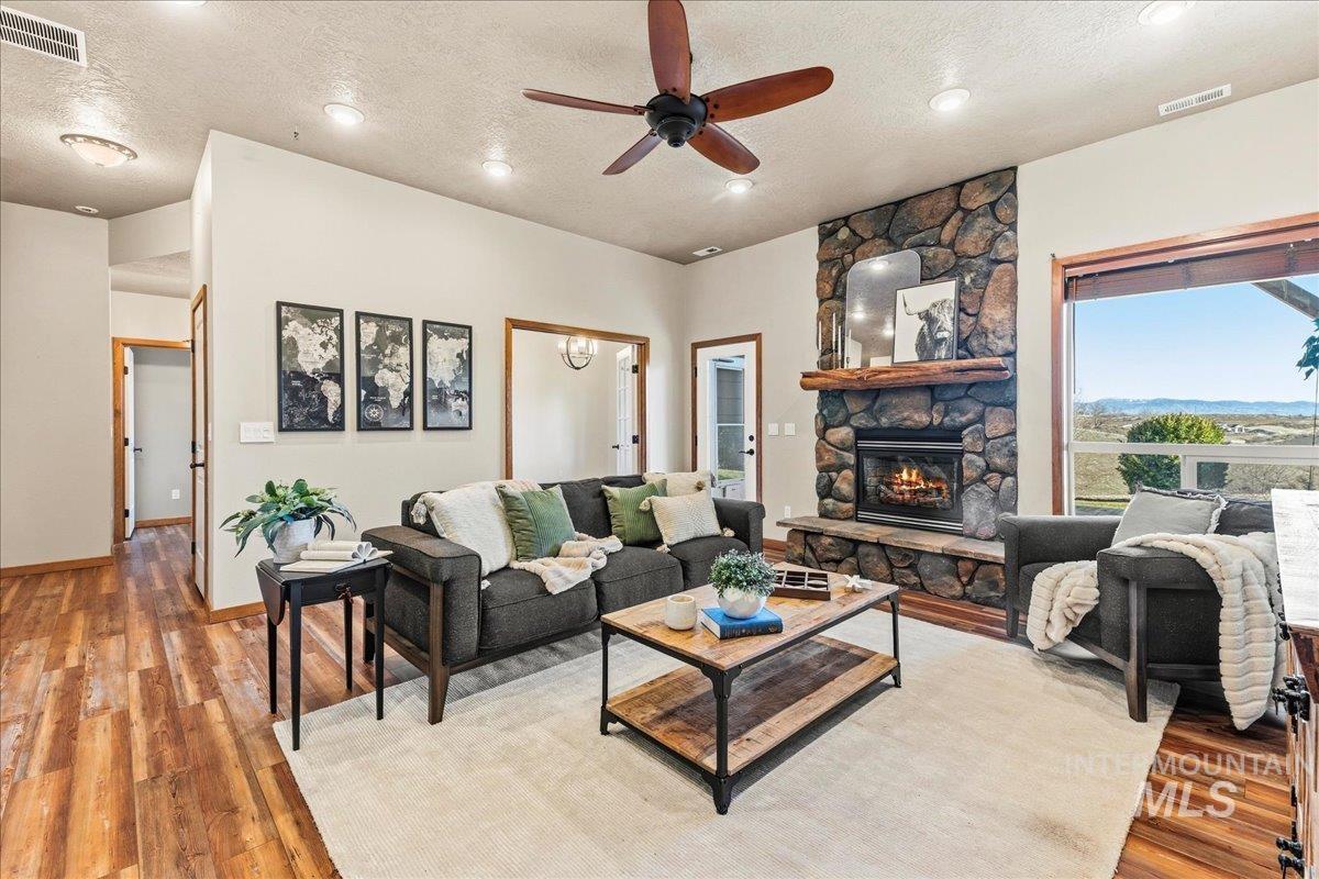 Living area featuring a textured ceiling, a stone fireplace, wood finished floors, ceiling fan, and recessed lighting