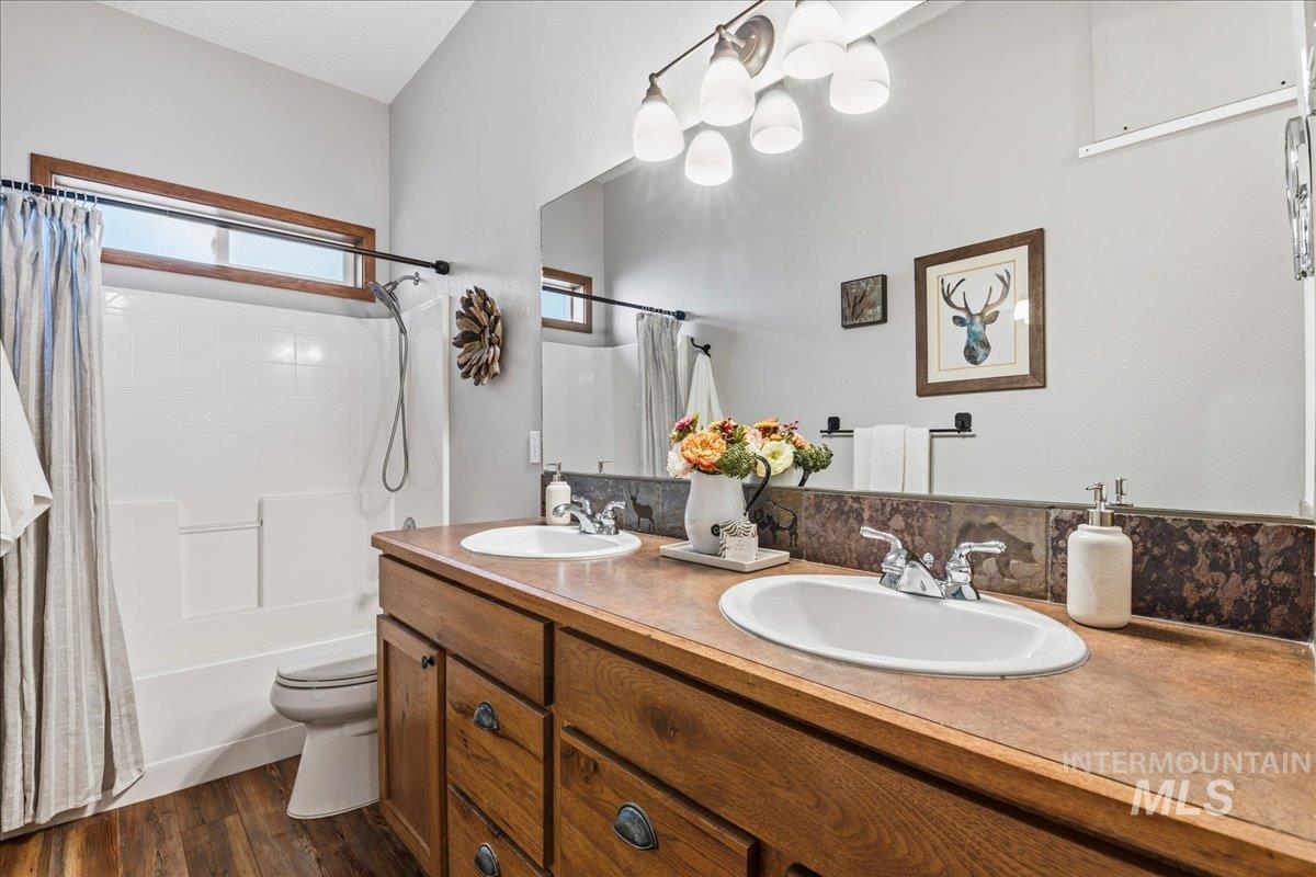 Bathroom featuring double vanity, shower / bath combination with curtain, and dark wood-style flooring