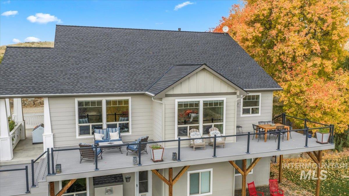 Rear view of house featuring board and batten siding, roof with shingles, outdoor dining area, and a deck