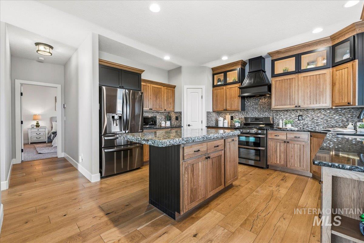 Kitchen featuring dark stone countertops, appliances with stainless steel finishes, a center island, tasteful backsplash, and premium range hood