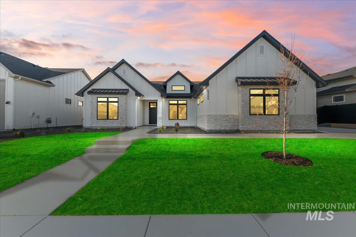 Modern inspired farmhouse featuring board and batten siding, a standing seam roof, a front yard, a metal roof, and stone siding
