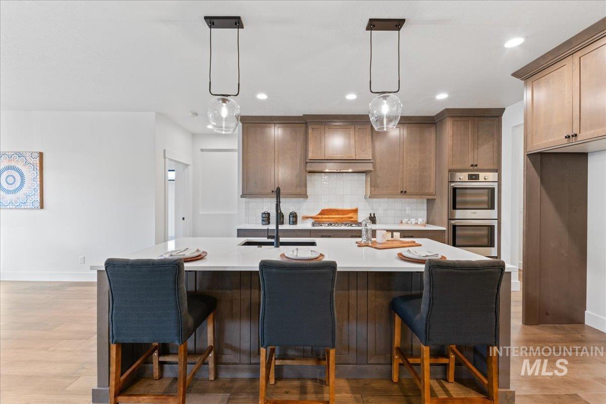 Kitchen with hanging light fixtures, a kitchen bar, tasteful backsplash, stainless steel double oven, and an island with sink