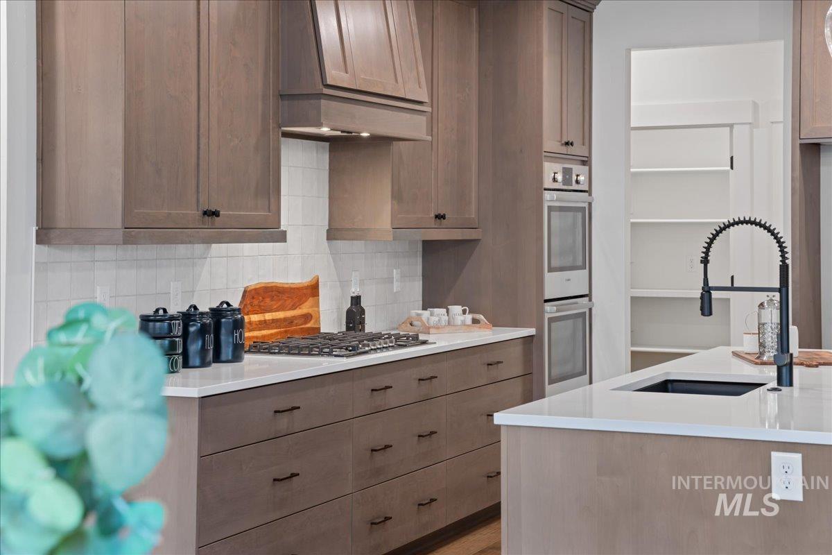 Kitchen featuring backsplash, stainless steel appliances, light stone counters, and custom exhaust hood