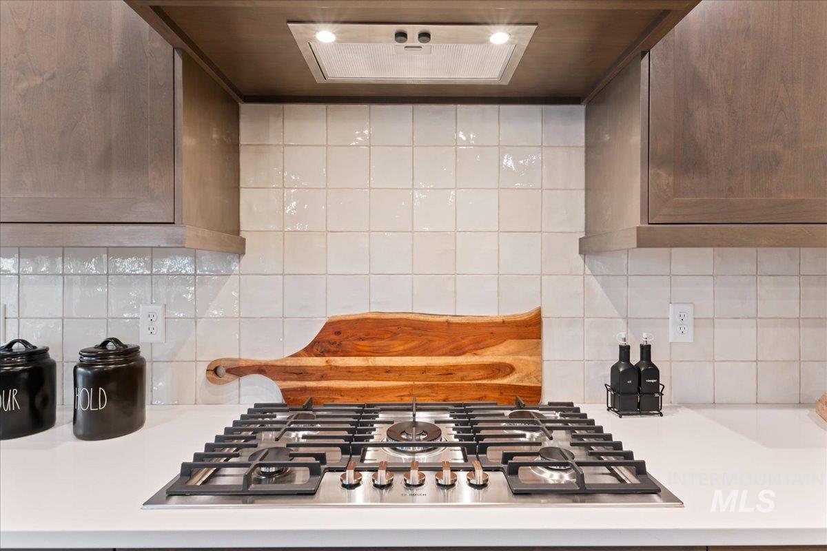 Kitchen view of ventilation hood, backsplash, and stainless steel gas cooktop